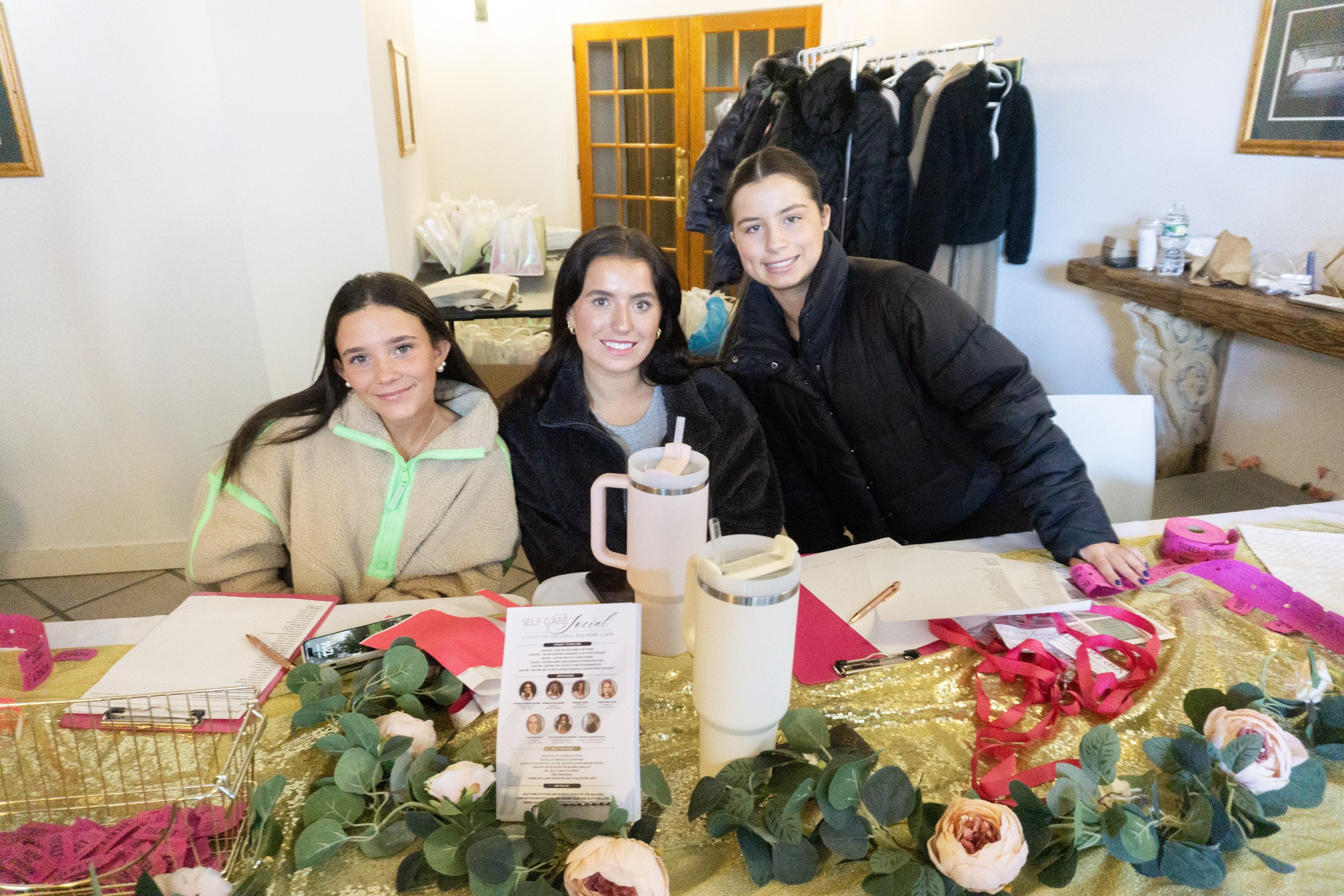 Three girls sitting at a decorated table with pink and gold accents, smiling at the camera.
