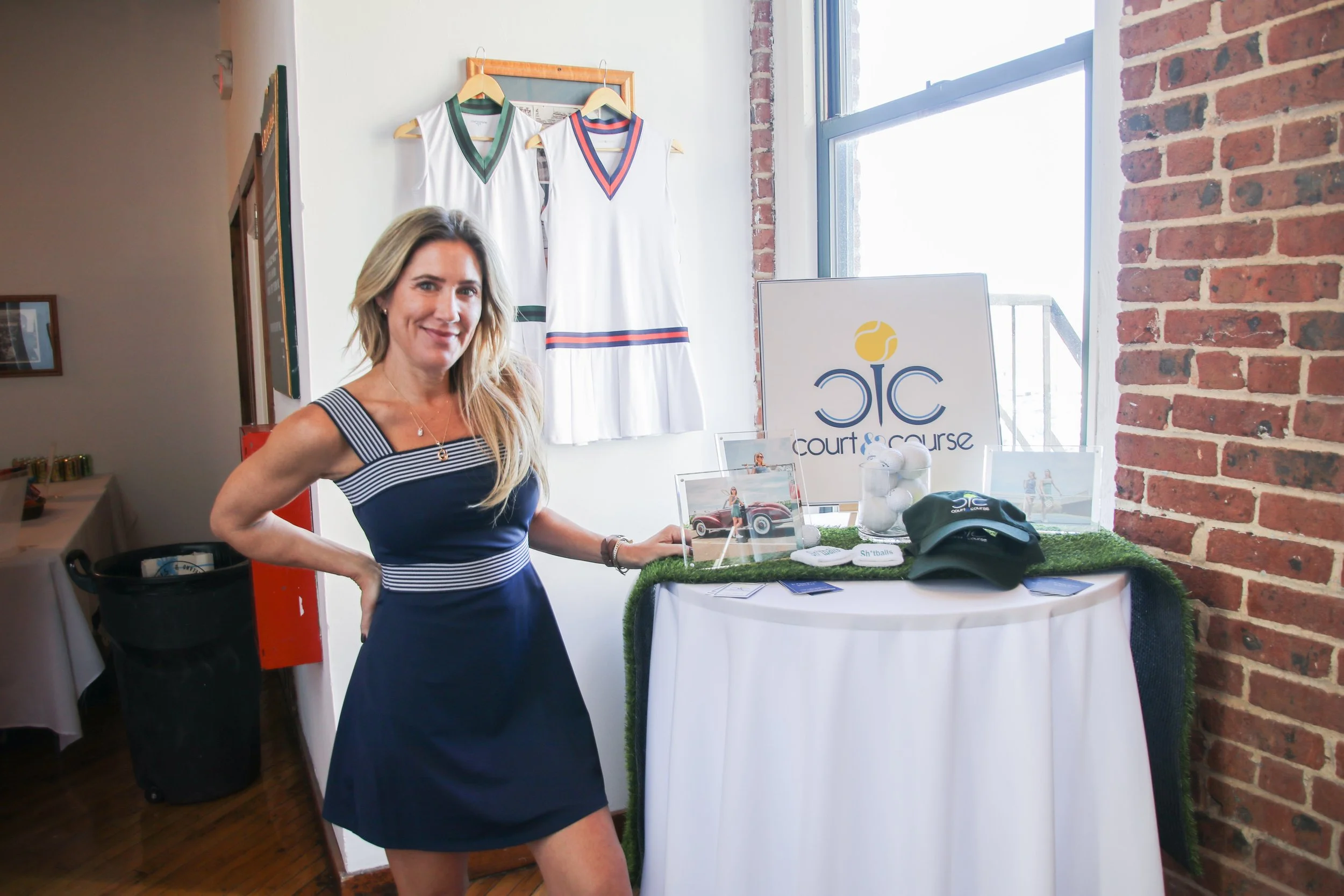 A woman posing next to a table with tennis equipment and promotional materials at an indoor event.