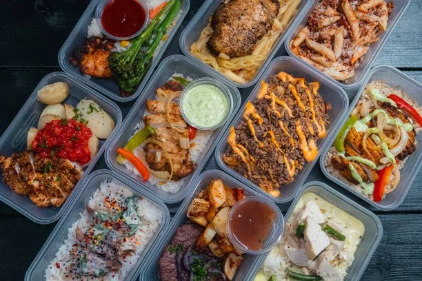 Multiple meals with various dishes, including pasta, chicken with vegetables, beef with sauce, rice with toppings, and dipping sauces on a dark table. Meals created to support you as you recover from illness, surgery or while postpartum