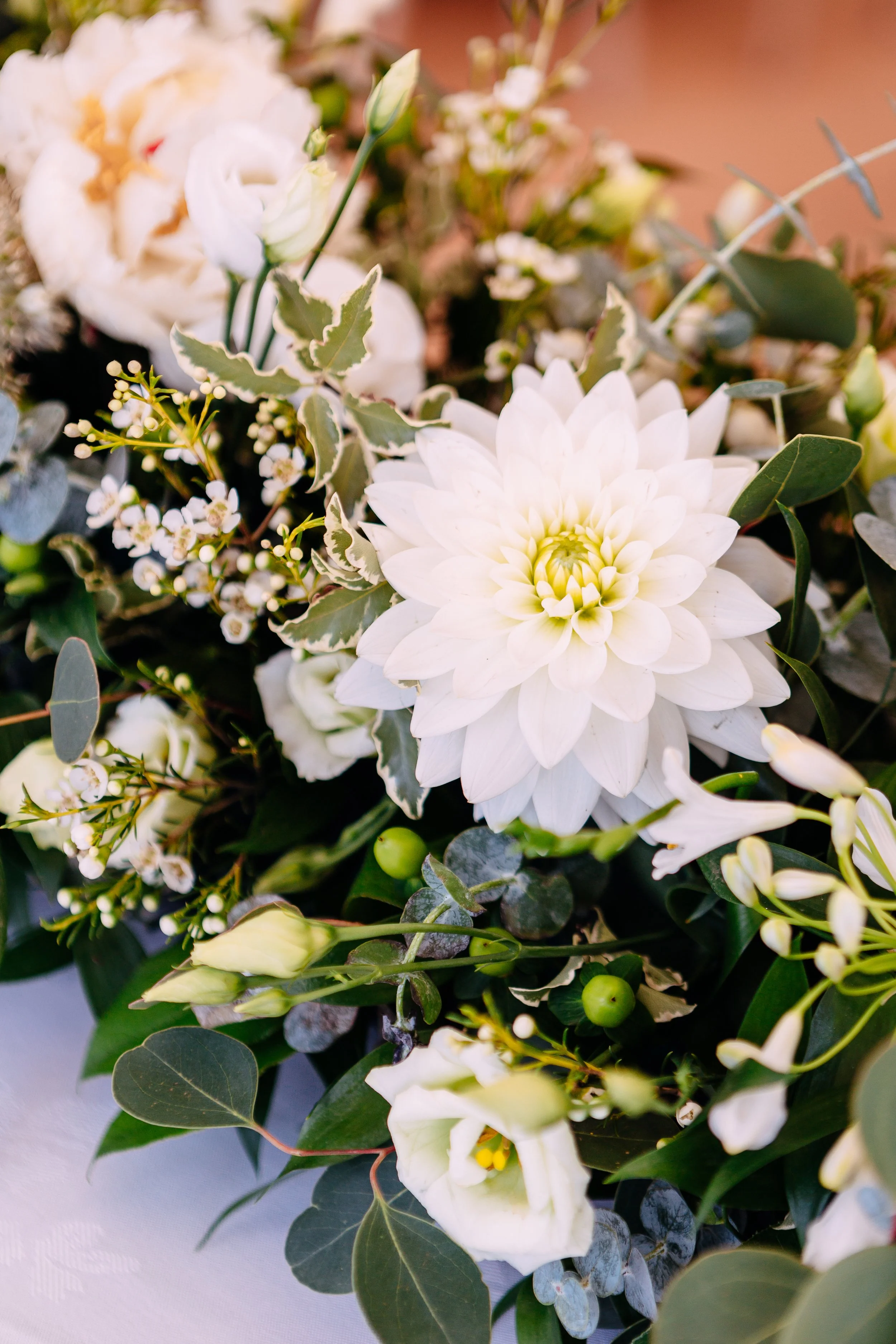 Close-up of a floral arrangement with white dahlias, eucalypt leaves, and small white filler flowers.