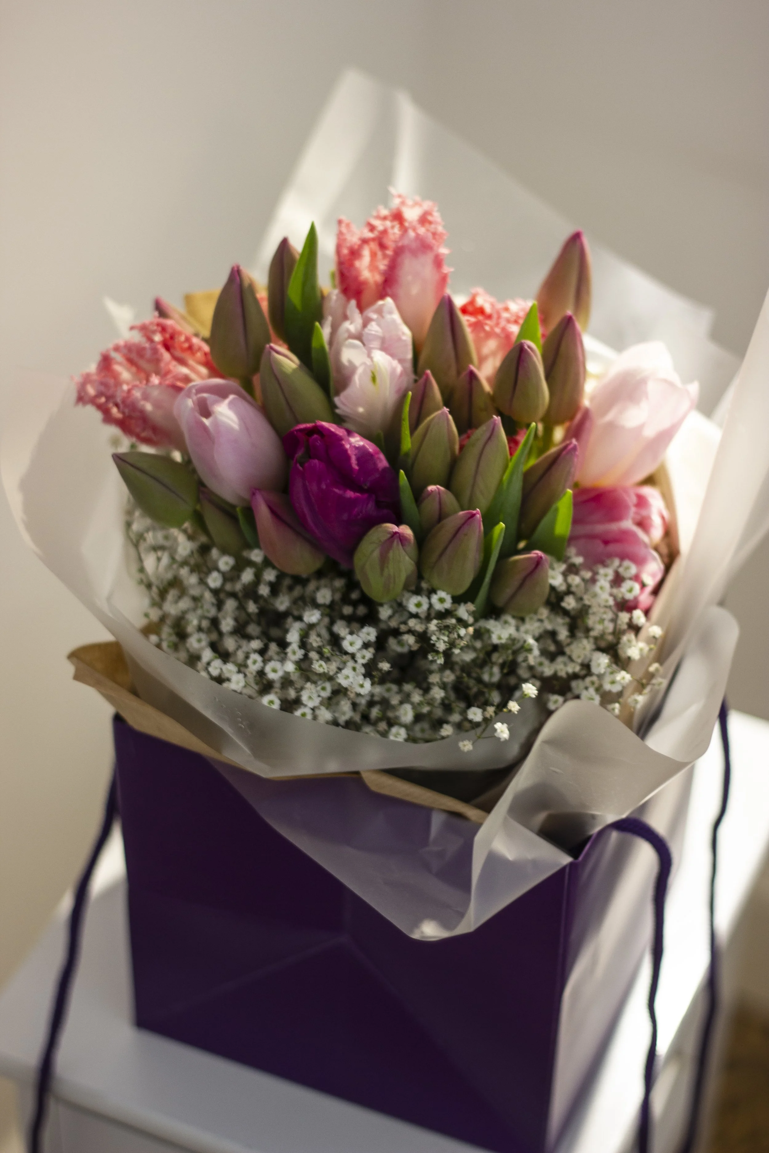 A bouquet of pink and white tulips and baby's breath in a purple gift bag.