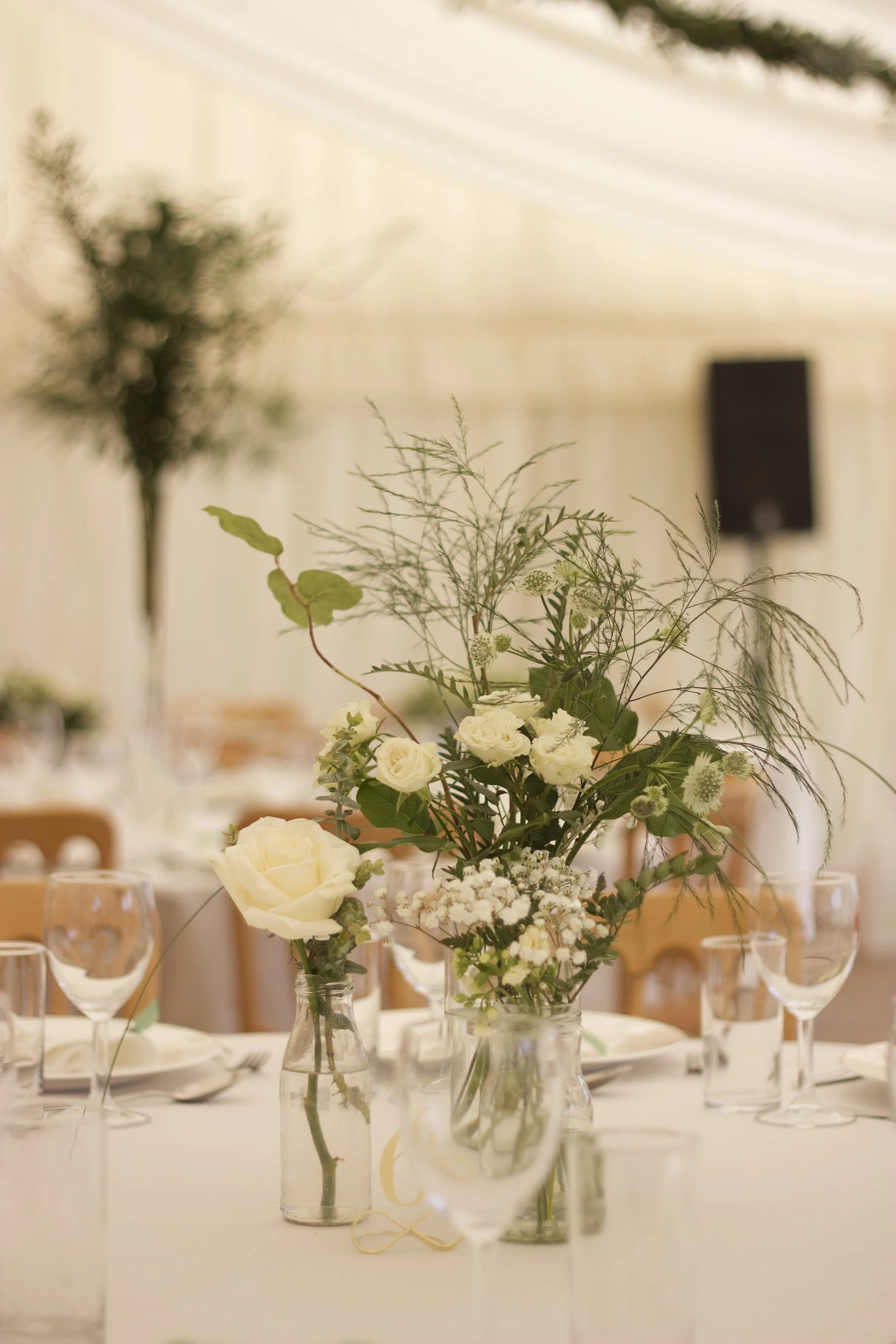 Elegant floral centerpiece with white roses, baby's breath, and greenery on a table set for a formal event.