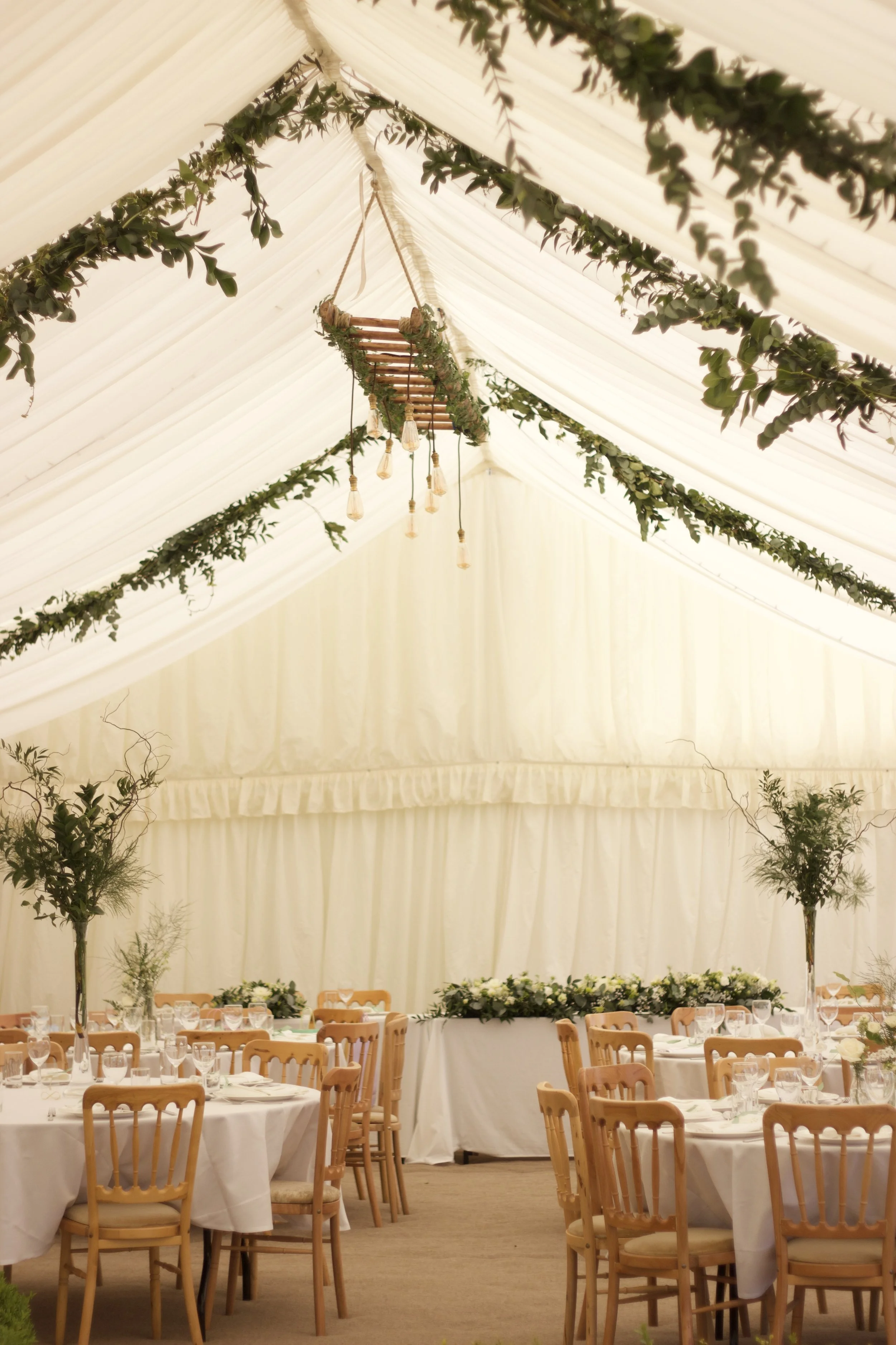 Inside a decorated event tent with tables, chairs, and floral centerpieces for a celebration or wedding.