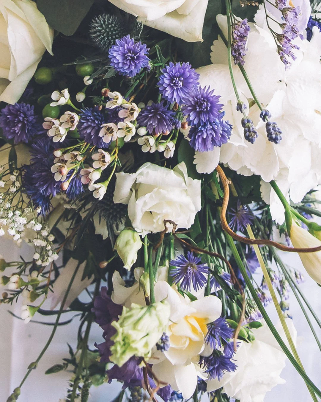 A bouquet of white, purple, and blue flowers, including white roses and purple chrysanthemums, with green stems and leaves.