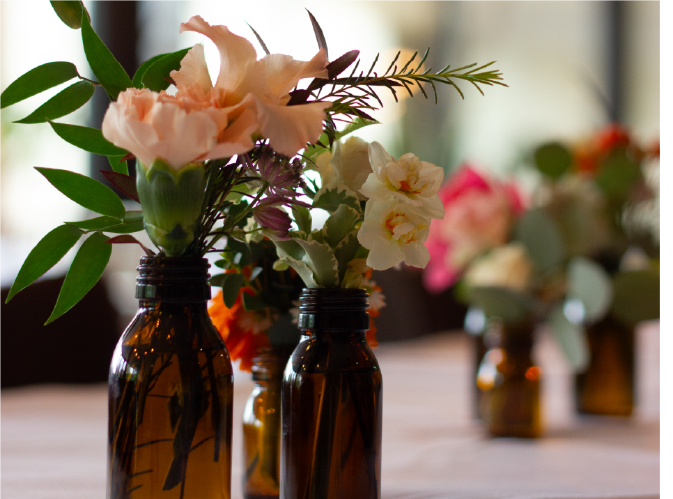 Small glass jar with white flowers and greenery on a wooden surface.