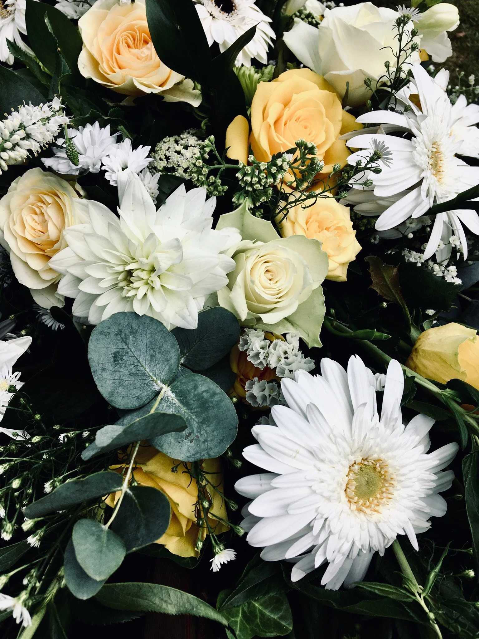 A bouquet of white and cream-colored flowers including roses, daisies, and a dahlia, with green foliage and eucalyptus leaves.
