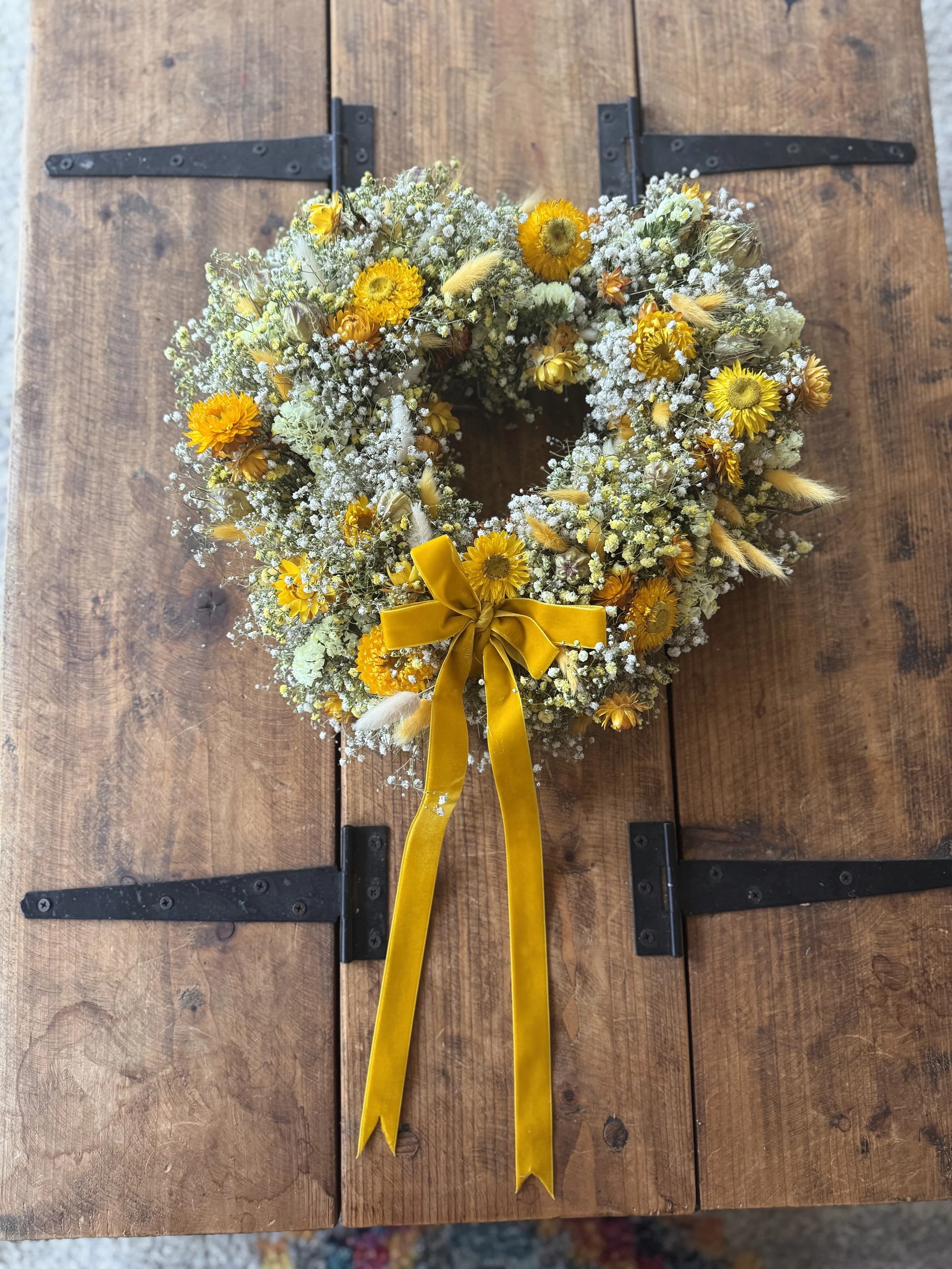 A yellow floral wreath with a yellow ribbon bow on a wooden surface.