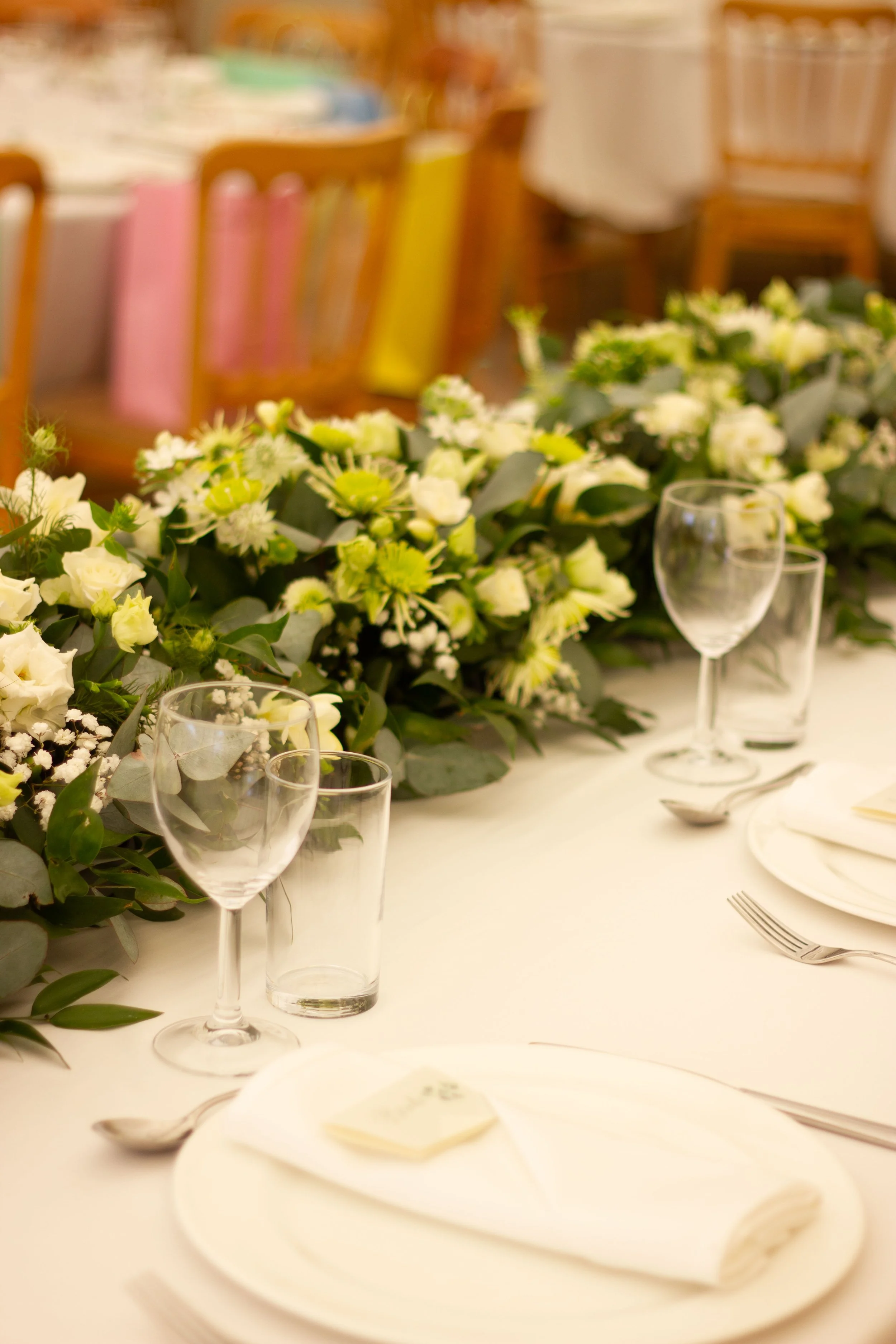 Elegant table setting with white plates, silverware, clear glassware, and a floral centerpiece with white and green flowers.