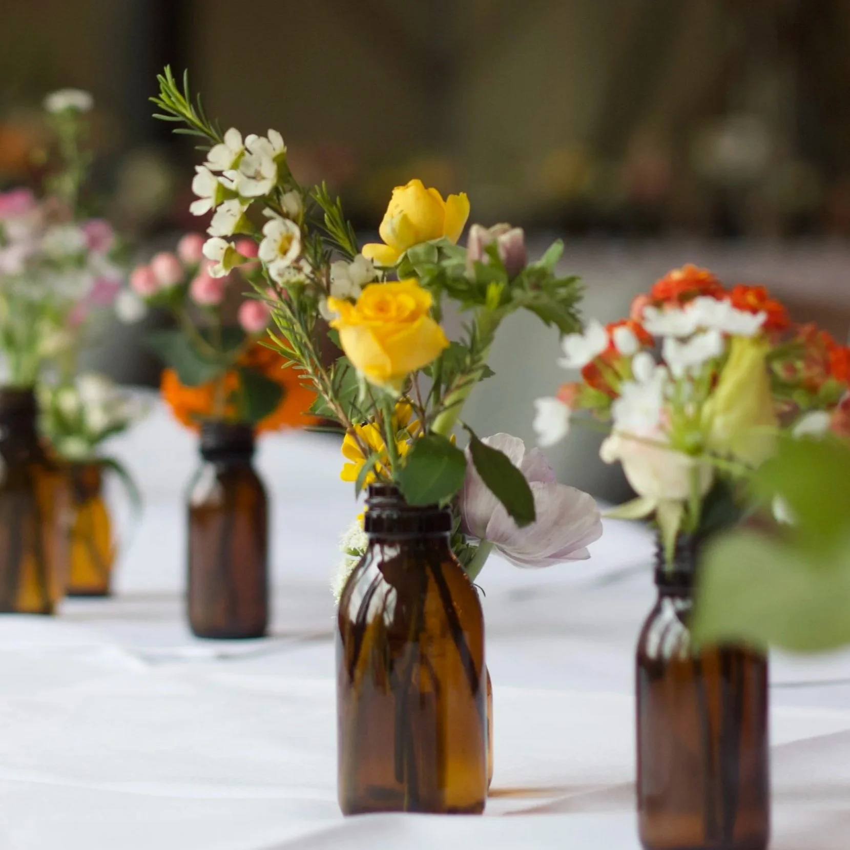 Brown glass bottles with colorful flower arrangements on a white tablecloth.
