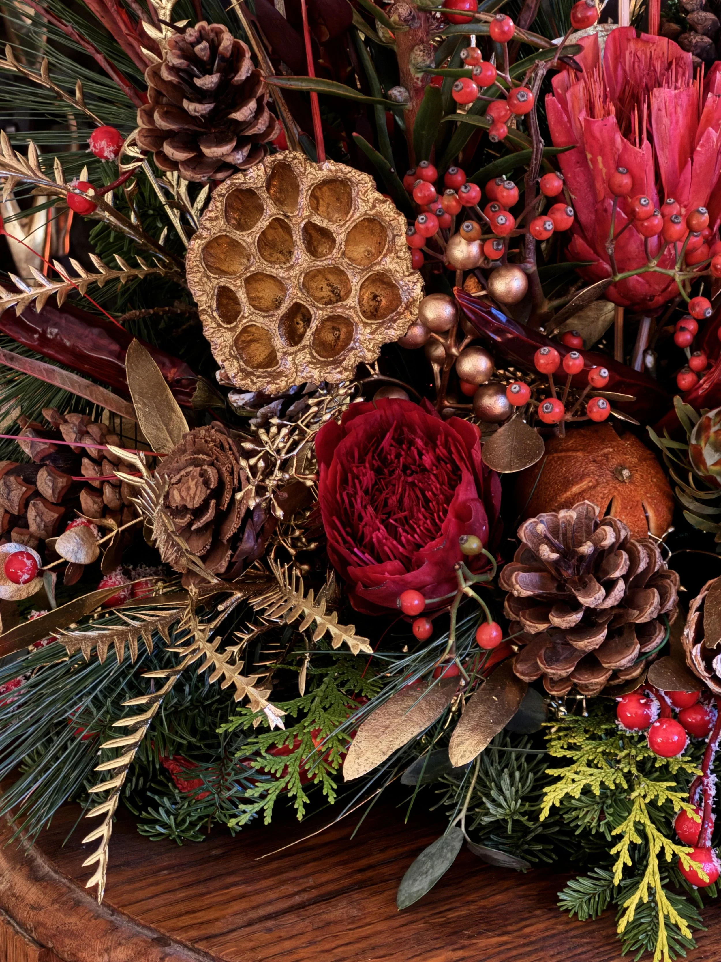 A decorative arrangement of red flowers, pinecones, berries, and metallic and dried botanical elements.