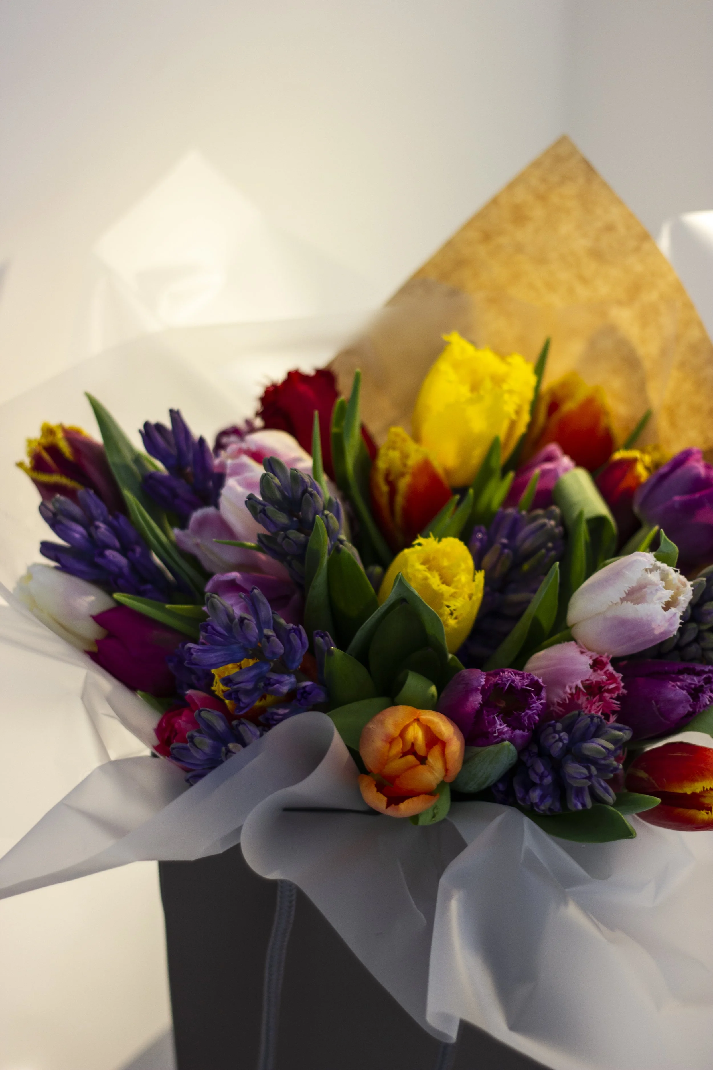 Colorful bouquet of various flowers including tulips, hyacinths, and other blossoms wrapped in white and brown paper.