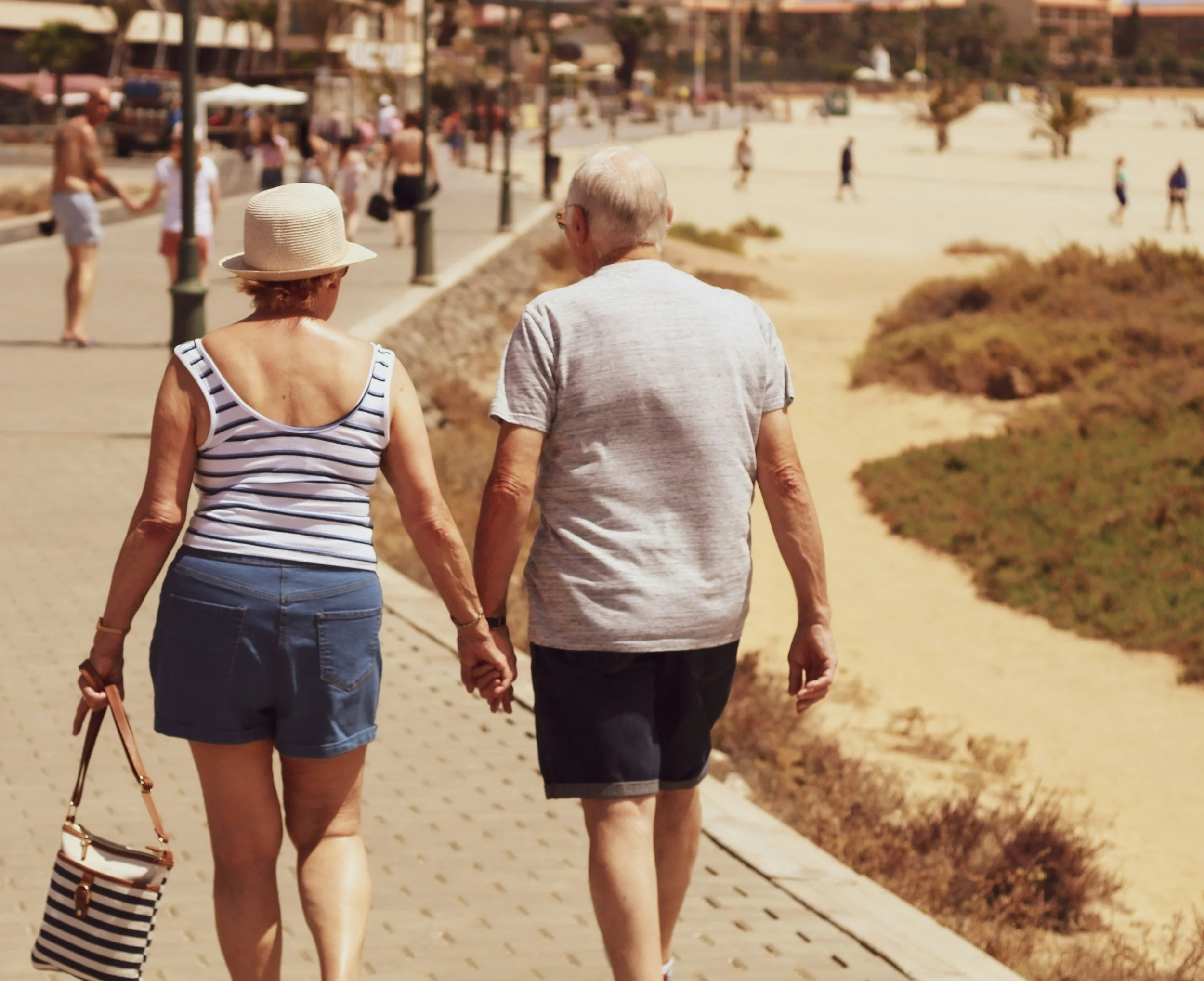 Elderly couple holding hands walking on a beachside path