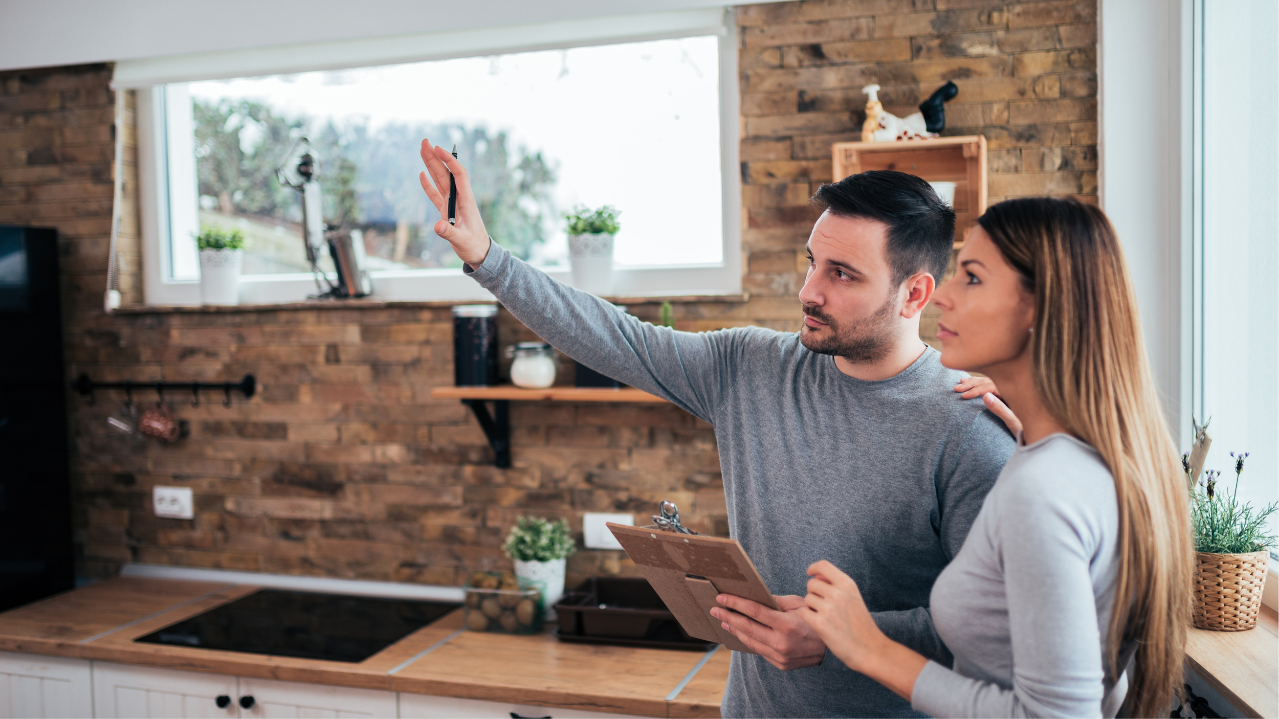 A man and woman in a kitchen, with the man holding a pen and pointing to a tablet. The woman is holding the tablet and looking at where the man is pointing.