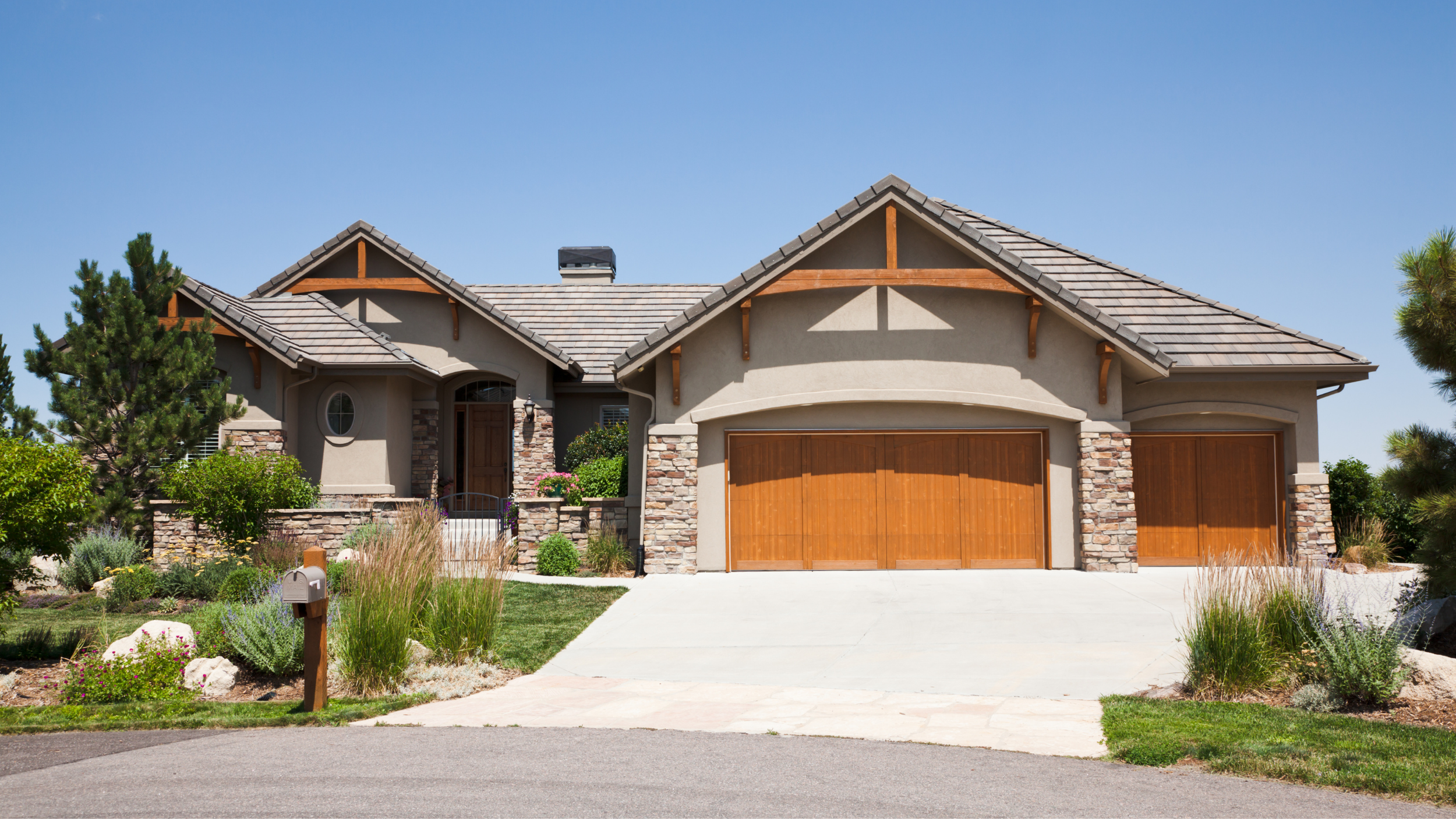 A modern suburban house with a three-car garage, stone and stucco exterior, and landscaped front yard under a clear blue sky.