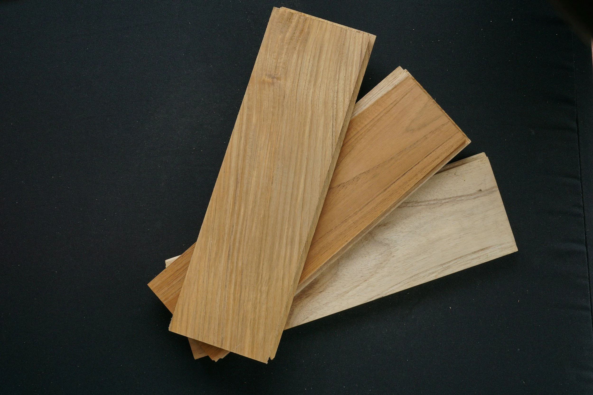 Three pieces of wood with different shades of natural wood grain, laid on a black surface. Engineered Hardwood and LVP