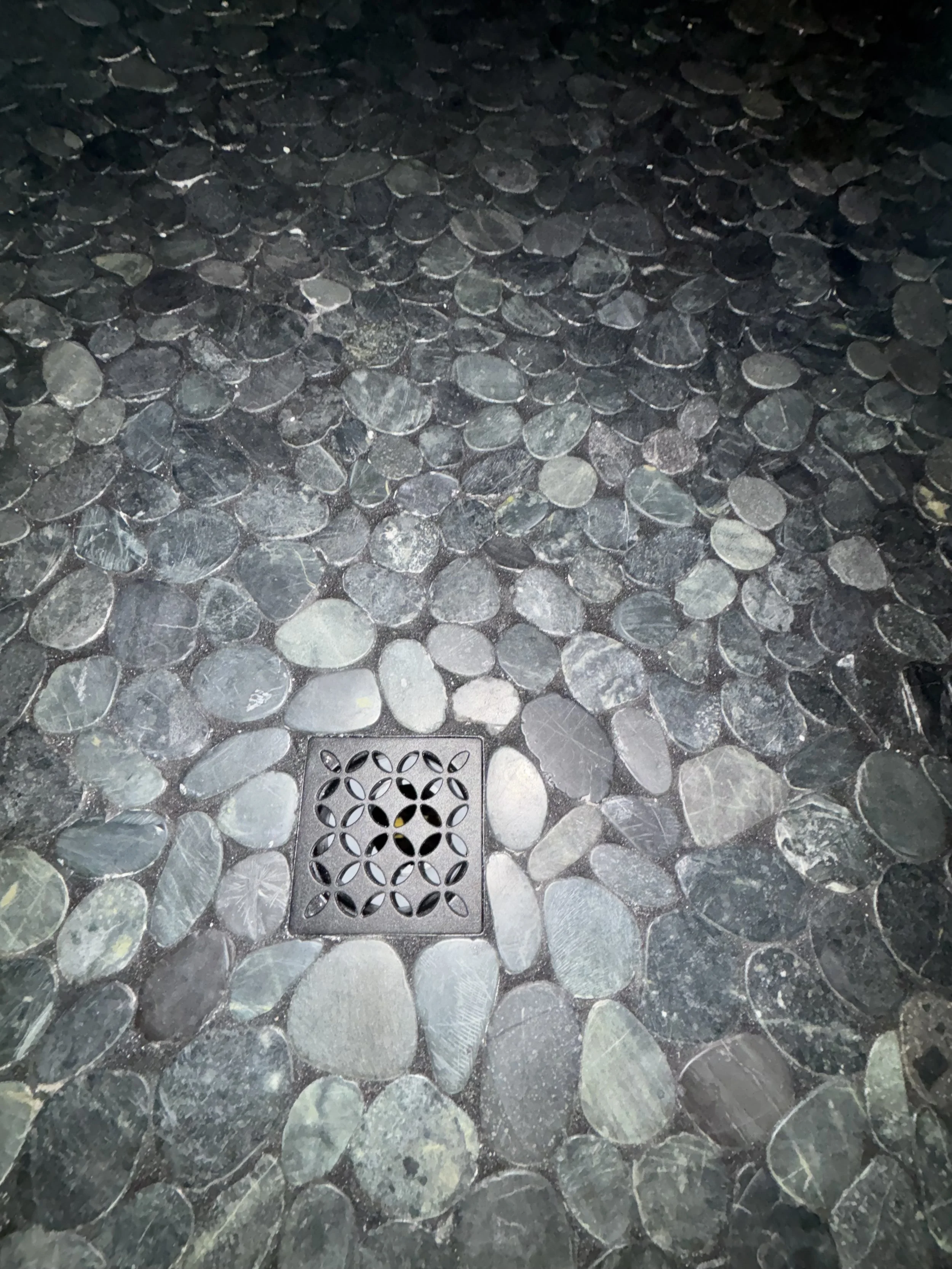Stone-tiled floor with a square metal drain cover in the center.