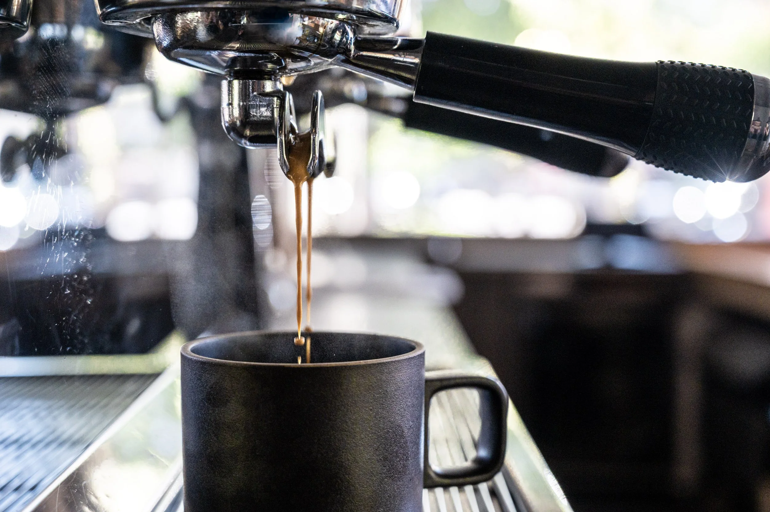Close-up of an espresso machine dispensing coffee into a black mug.