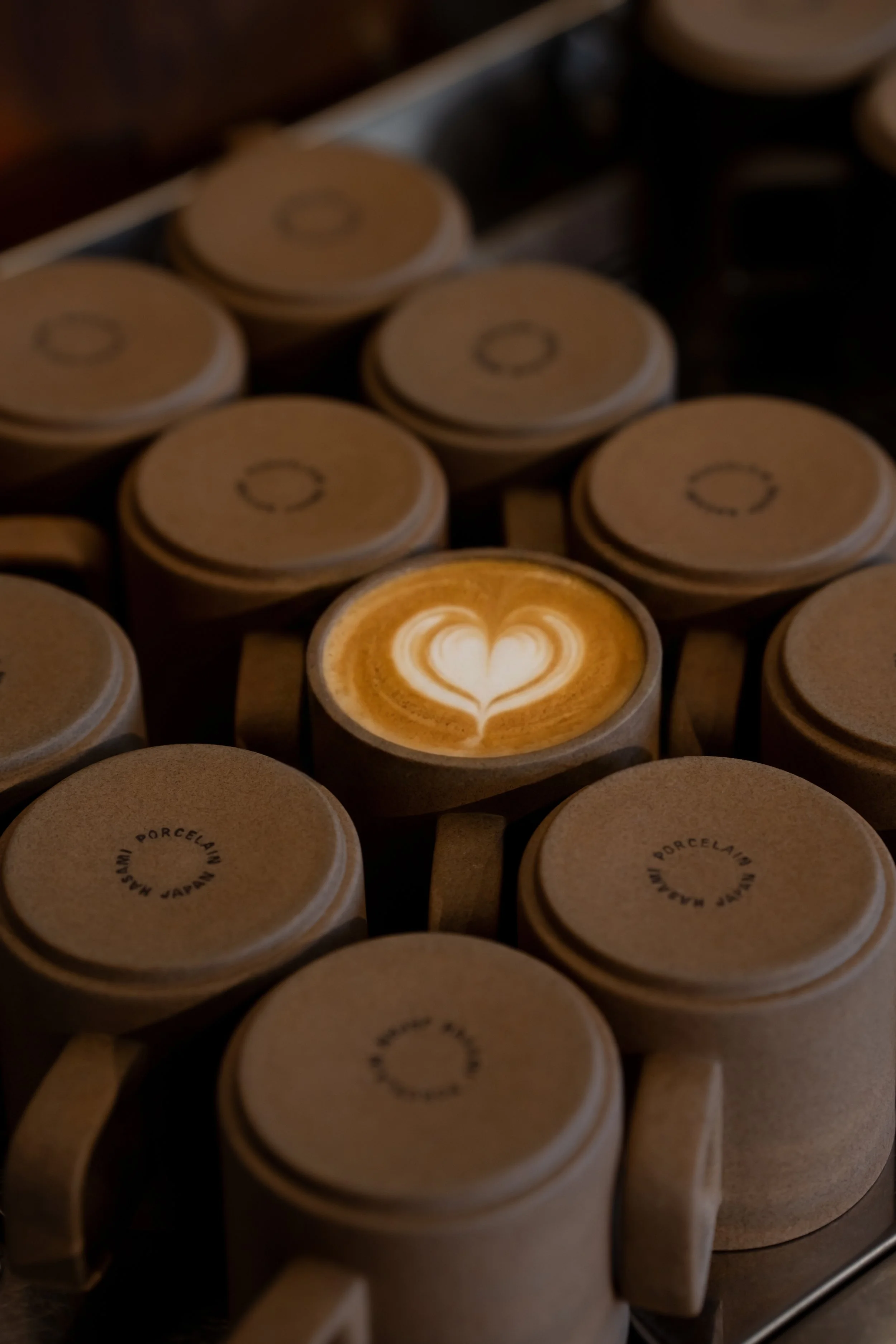 Top view of several beige coffee cups stacked upside down, with one cup showing a heart-shaped latte art design.