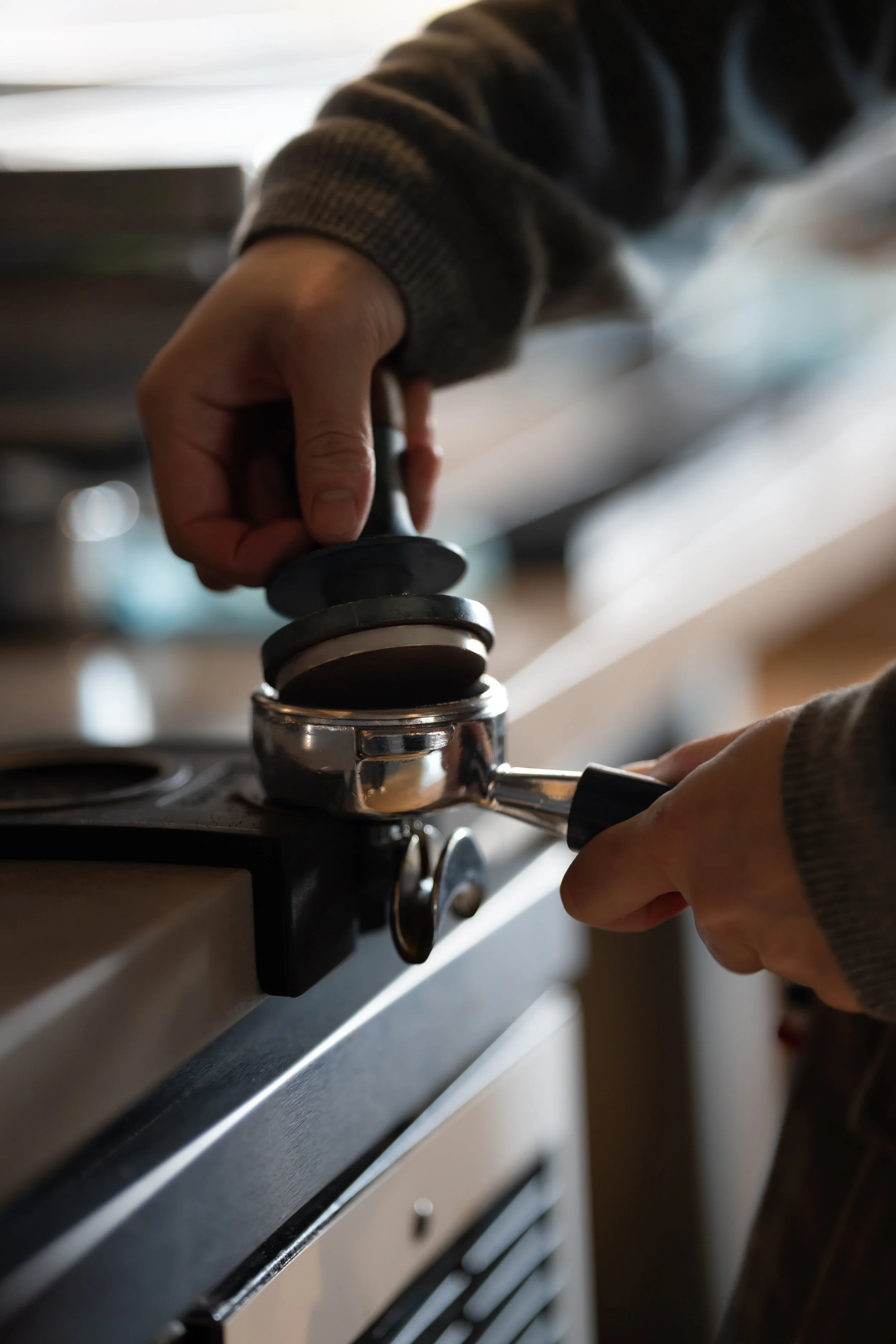 Person using a tamper to press coffee grounds in a portafilter on a stovetop