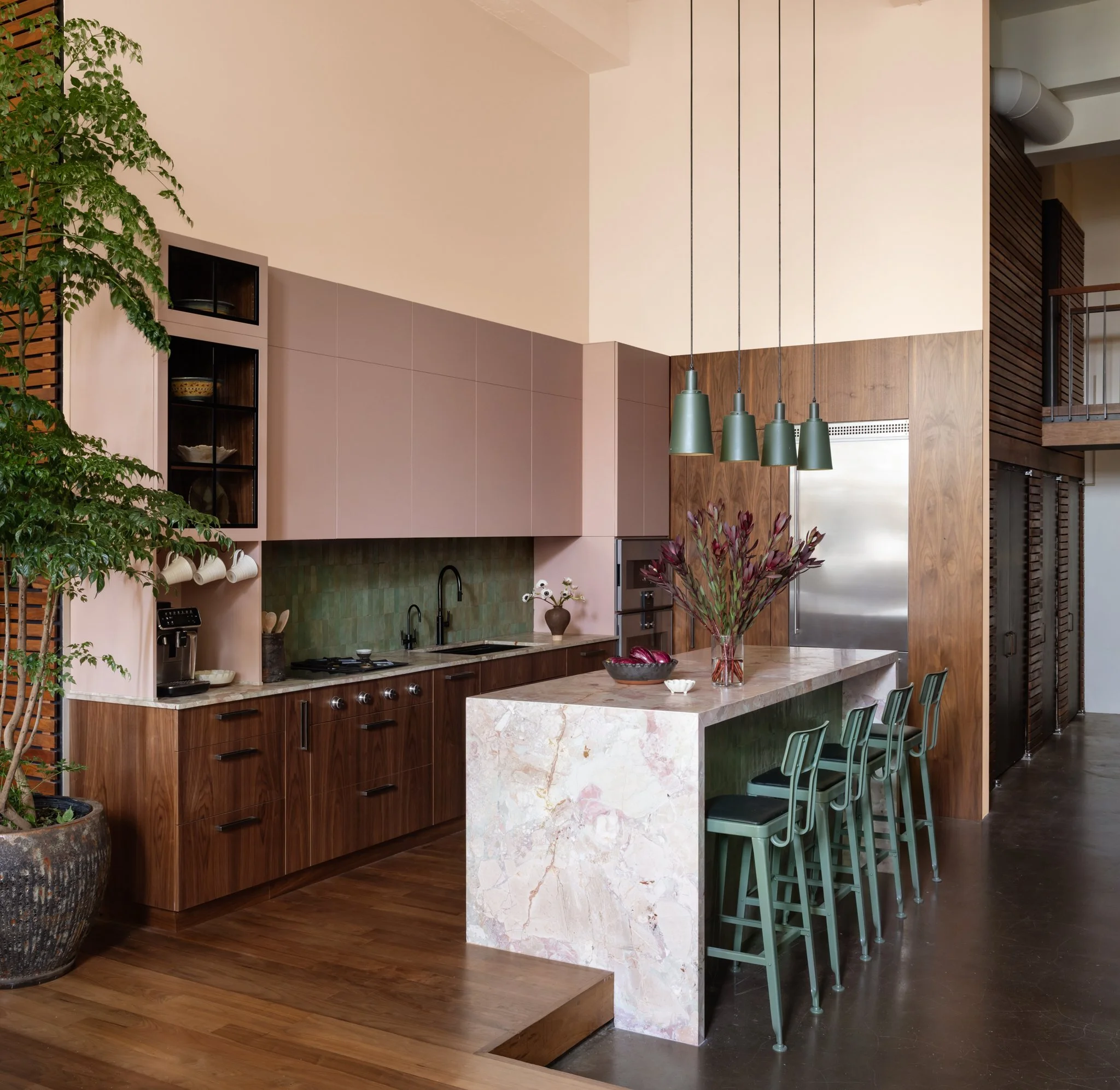 Modern kitchen with wood cabinets, marble island, green pendant lights, potted plant, and dining chairs.