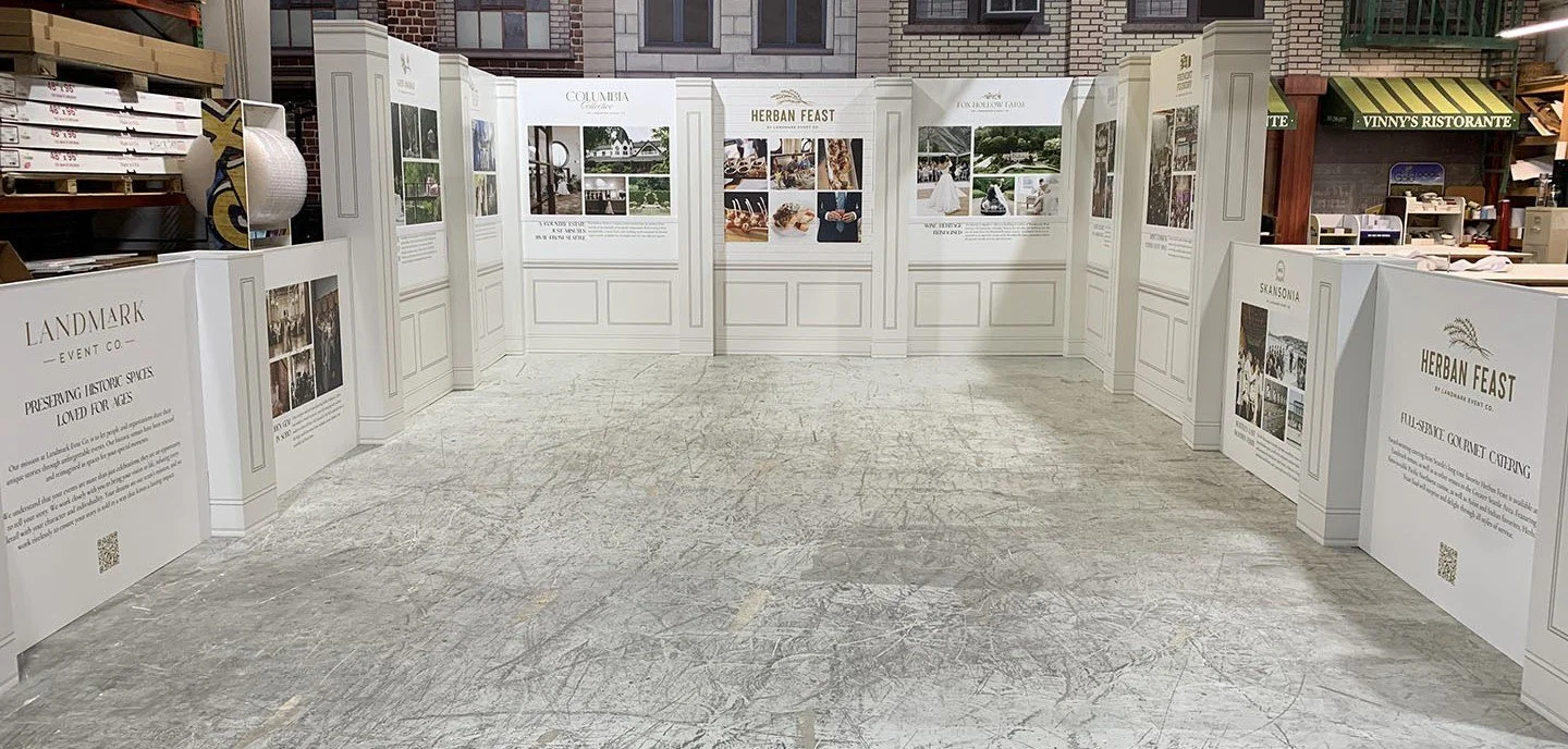 Indoor event display with panels promoting Landmark Event Co. and Herban Feast featuring images and text.