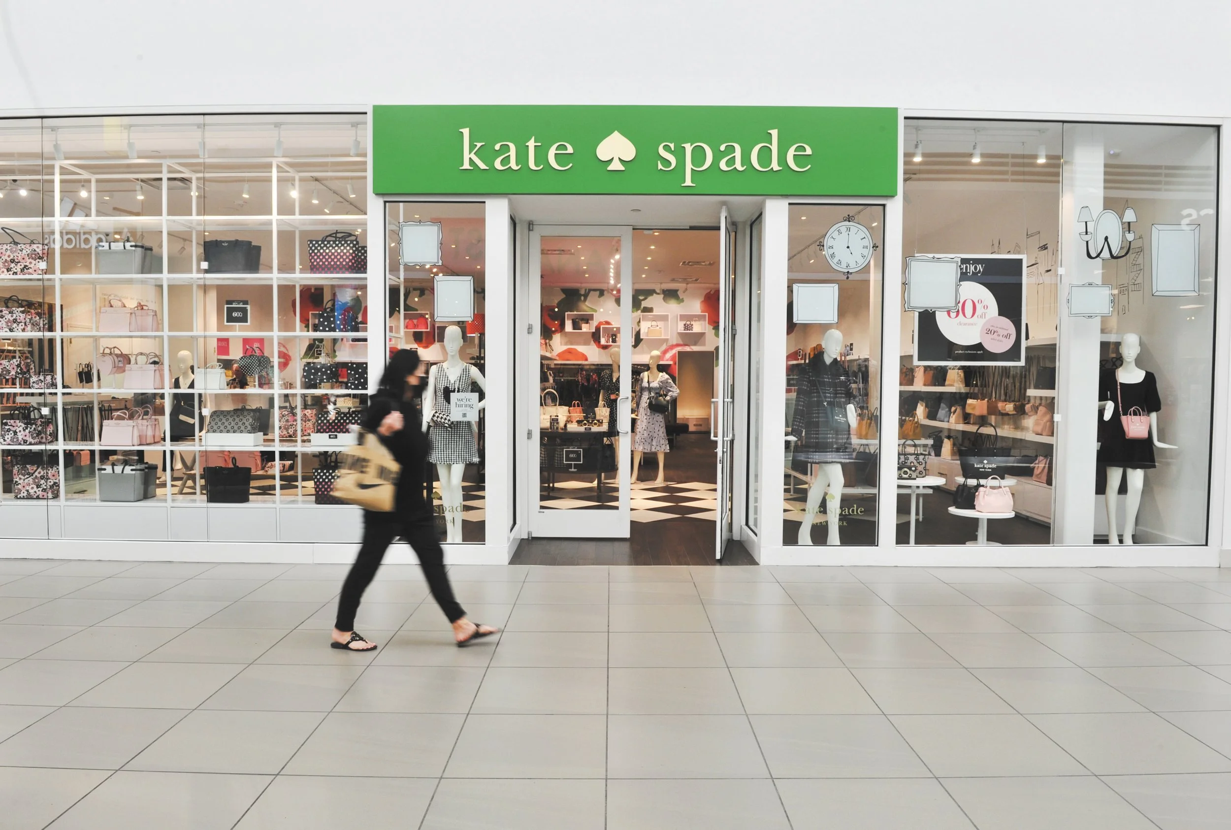 A person walking past a Kate Spade store with mannequins and handbags displayed.