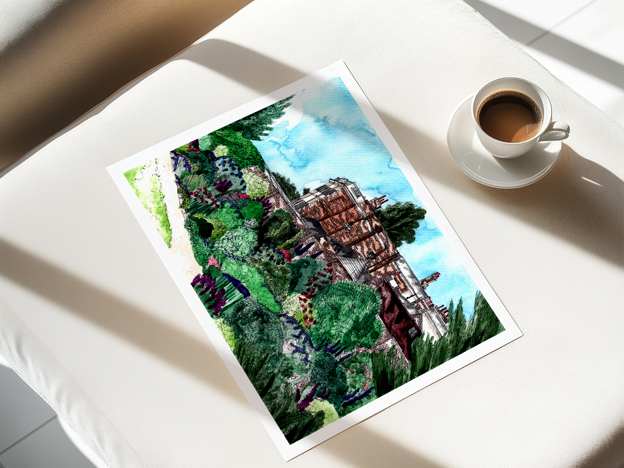 A watercolor painting of a traditional building surrounded by lush greenery and gardens, placed on a light-colored surface next to a cup of coffee.