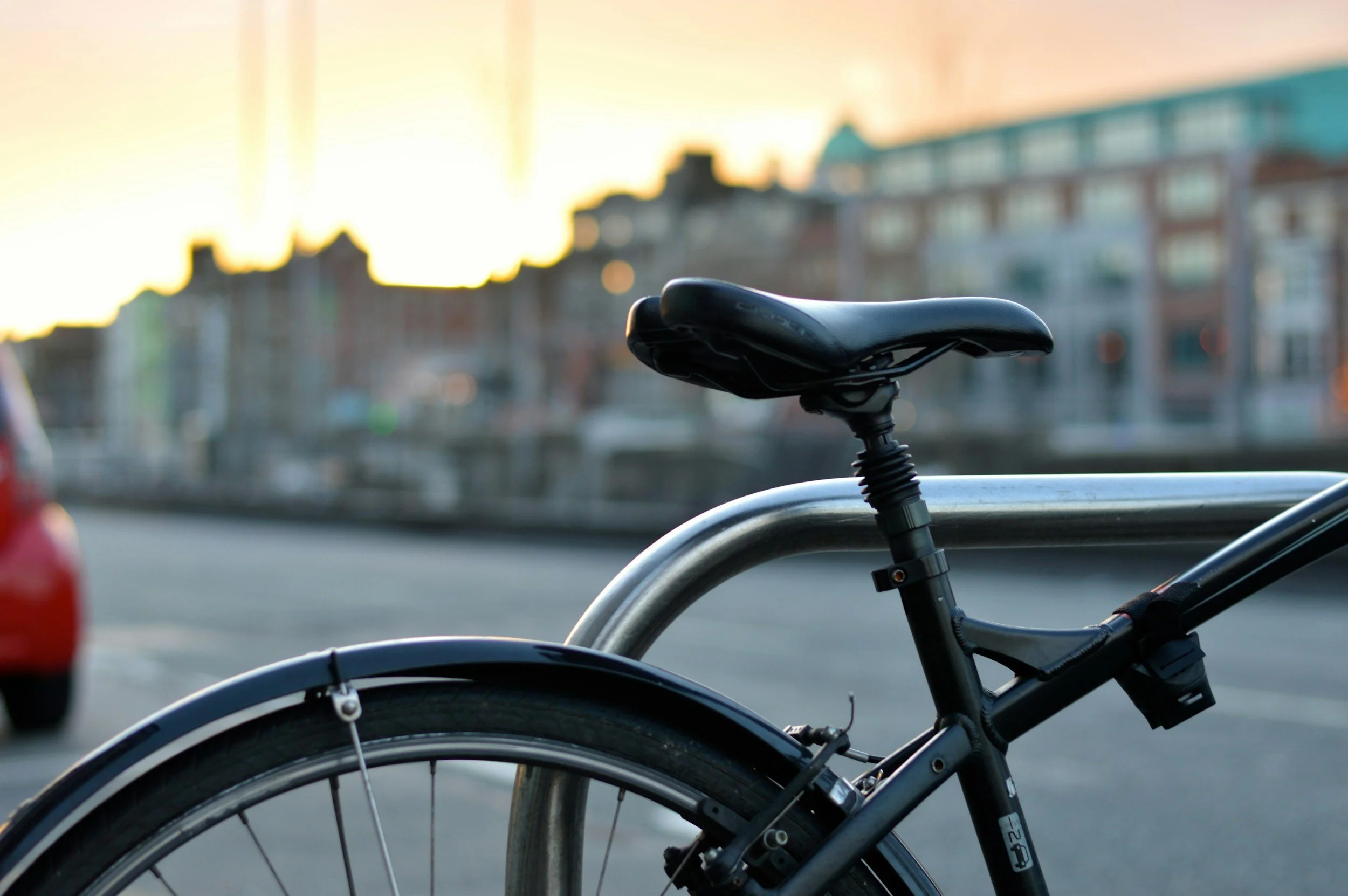 Bicycle seat and rear wheel are locked to a metal rail at sunset.