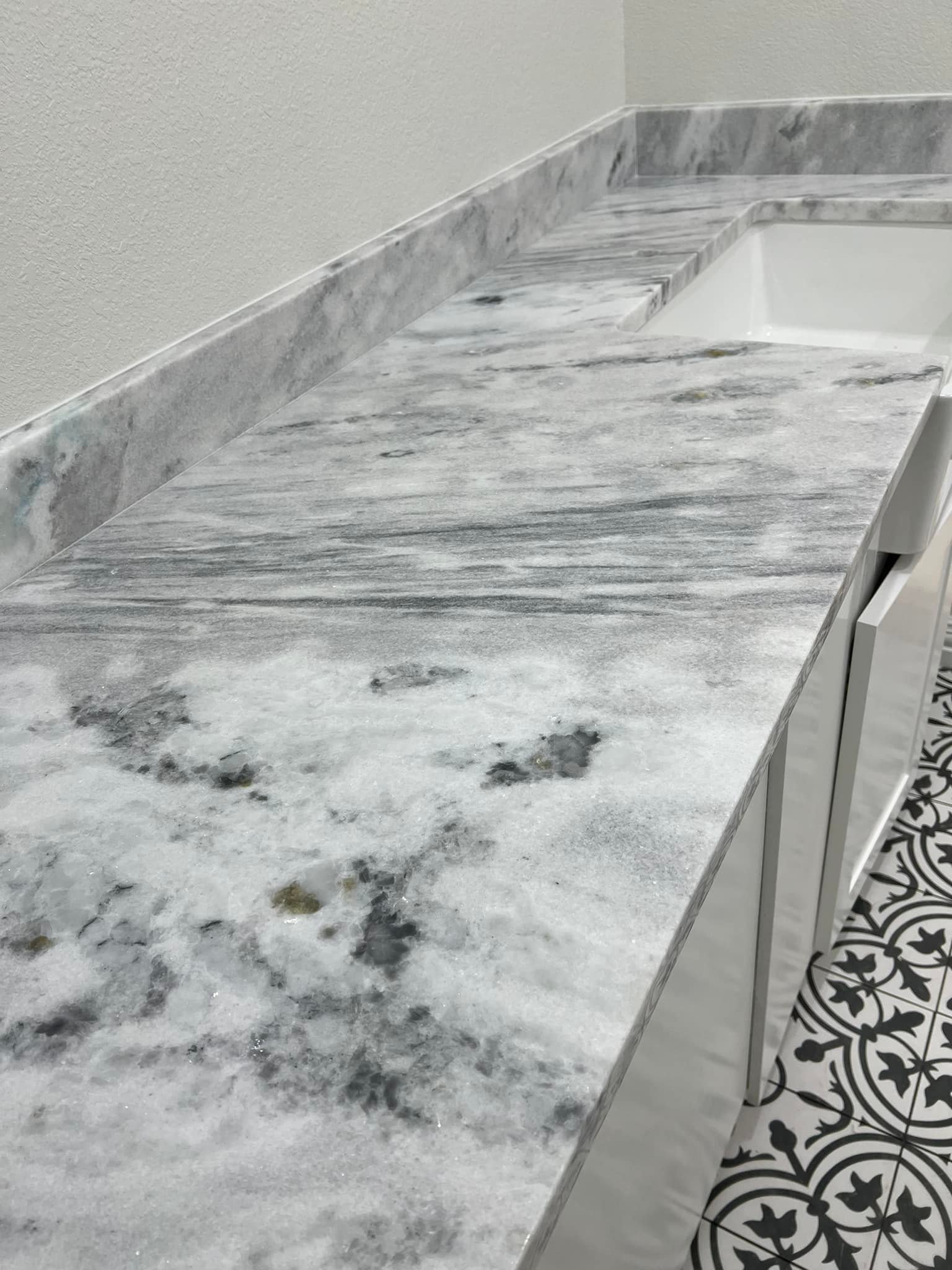 A gray and white marble countertop with a backsplash next to a white sink.