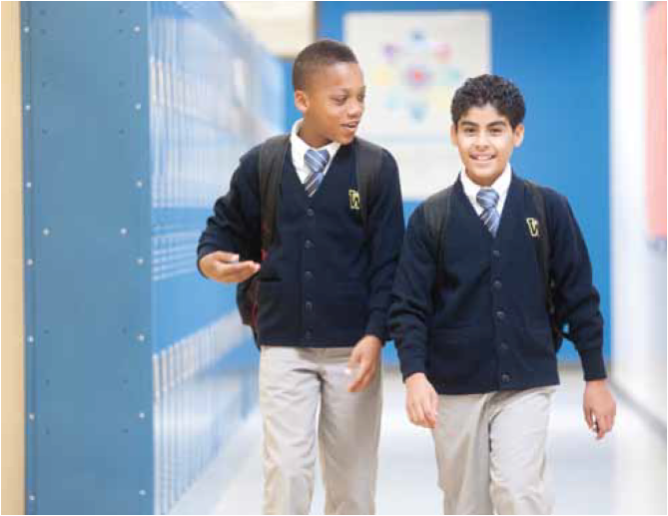 Two schoolboys in uniform walking and talking in an UpLift school hallway with blue lockers.