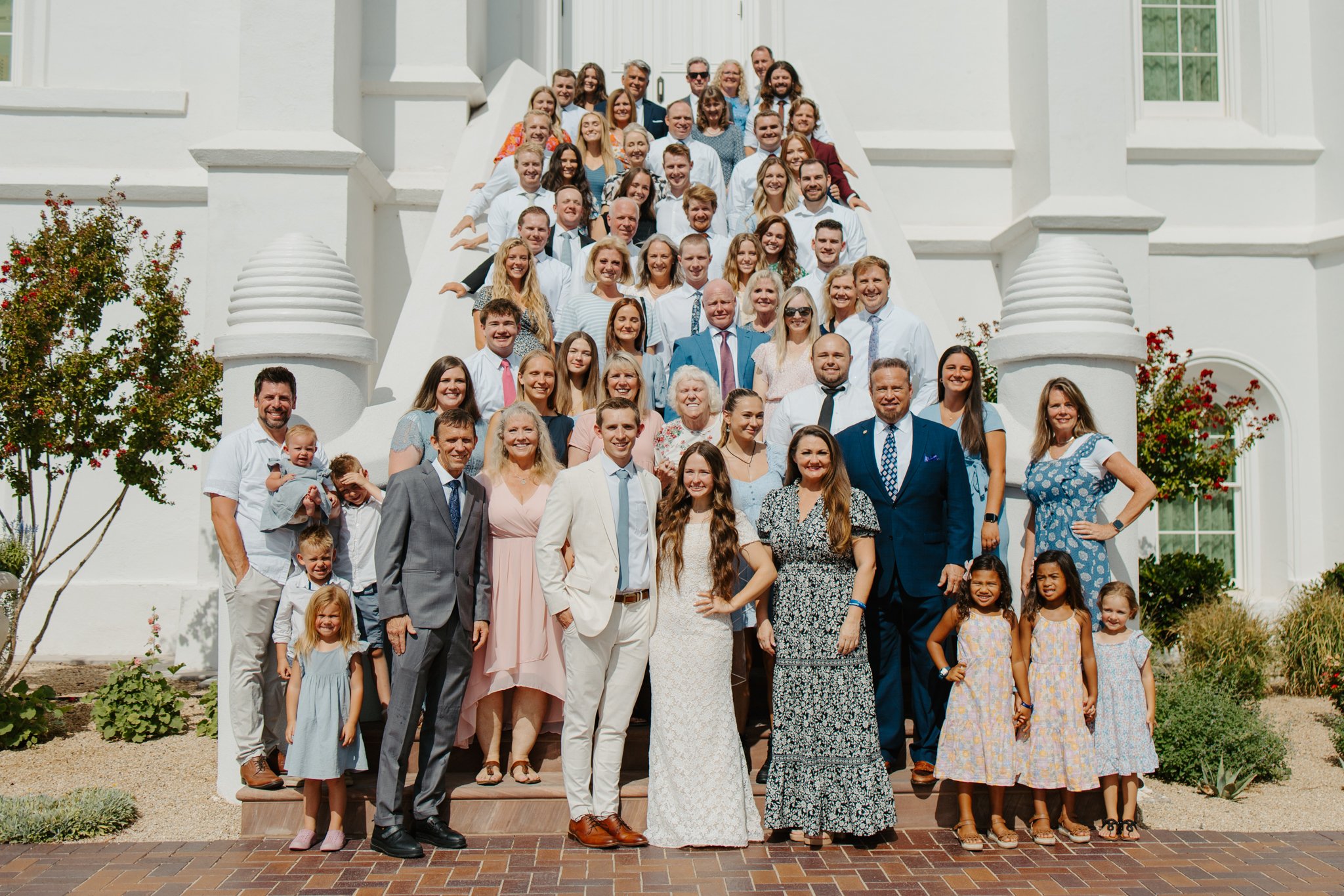A large group of people posing for a photo on steps outside a white building on a sunny day.