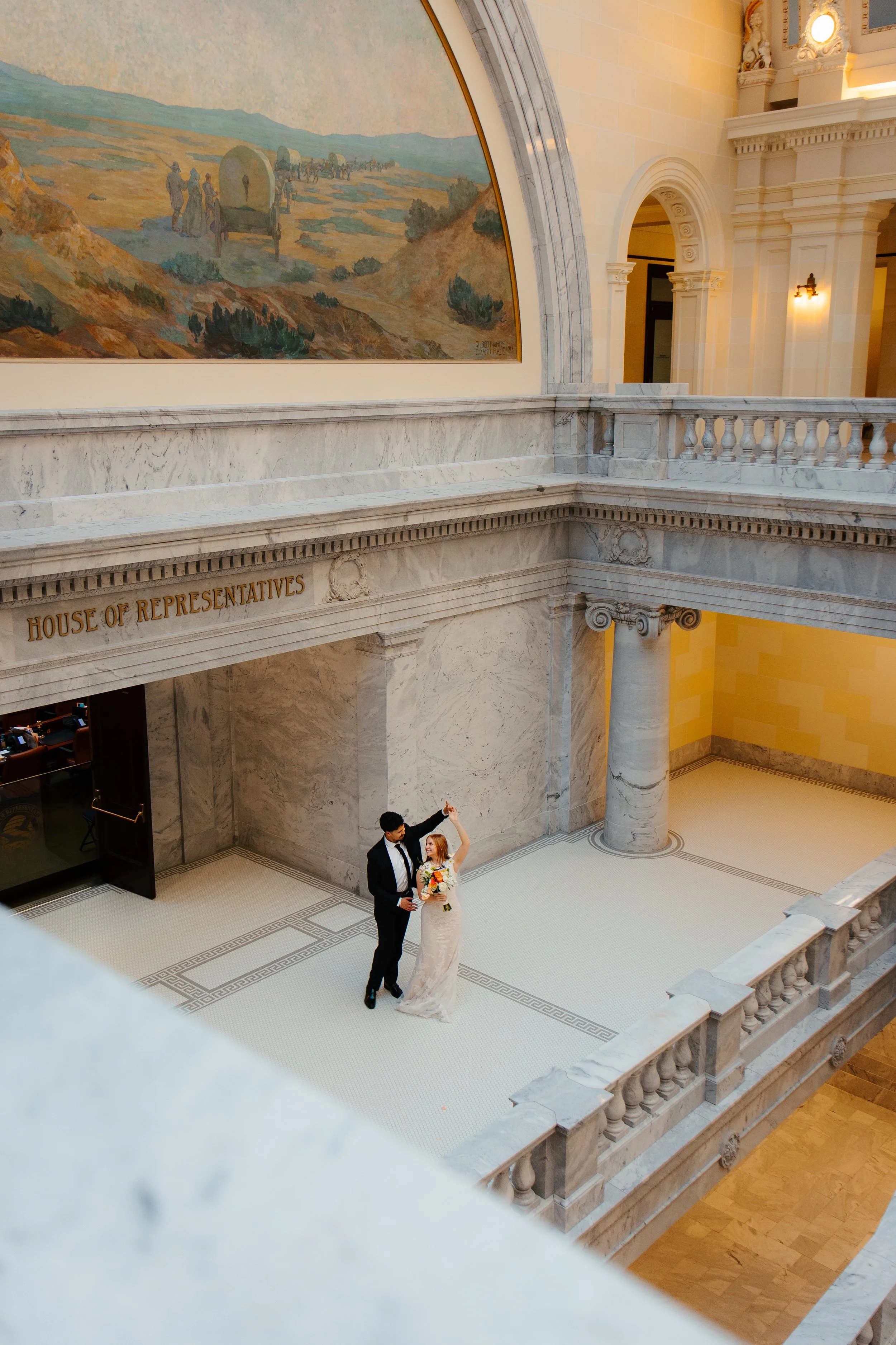 A bride and groom dancing inside a marble atrium of a government building, with the words 'House of Representatives' engraved on the marble railing.