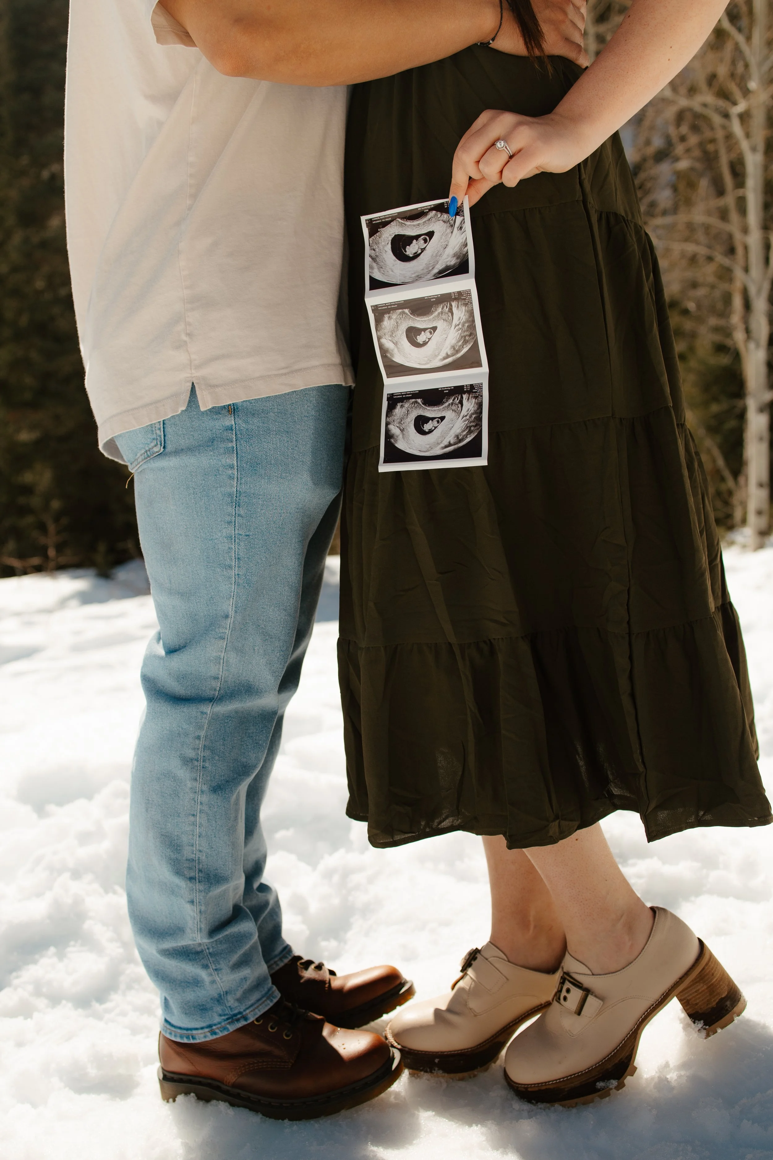 A couple standing in the snow, with the woman holding an ultrasound photo showing a developing fetus.
