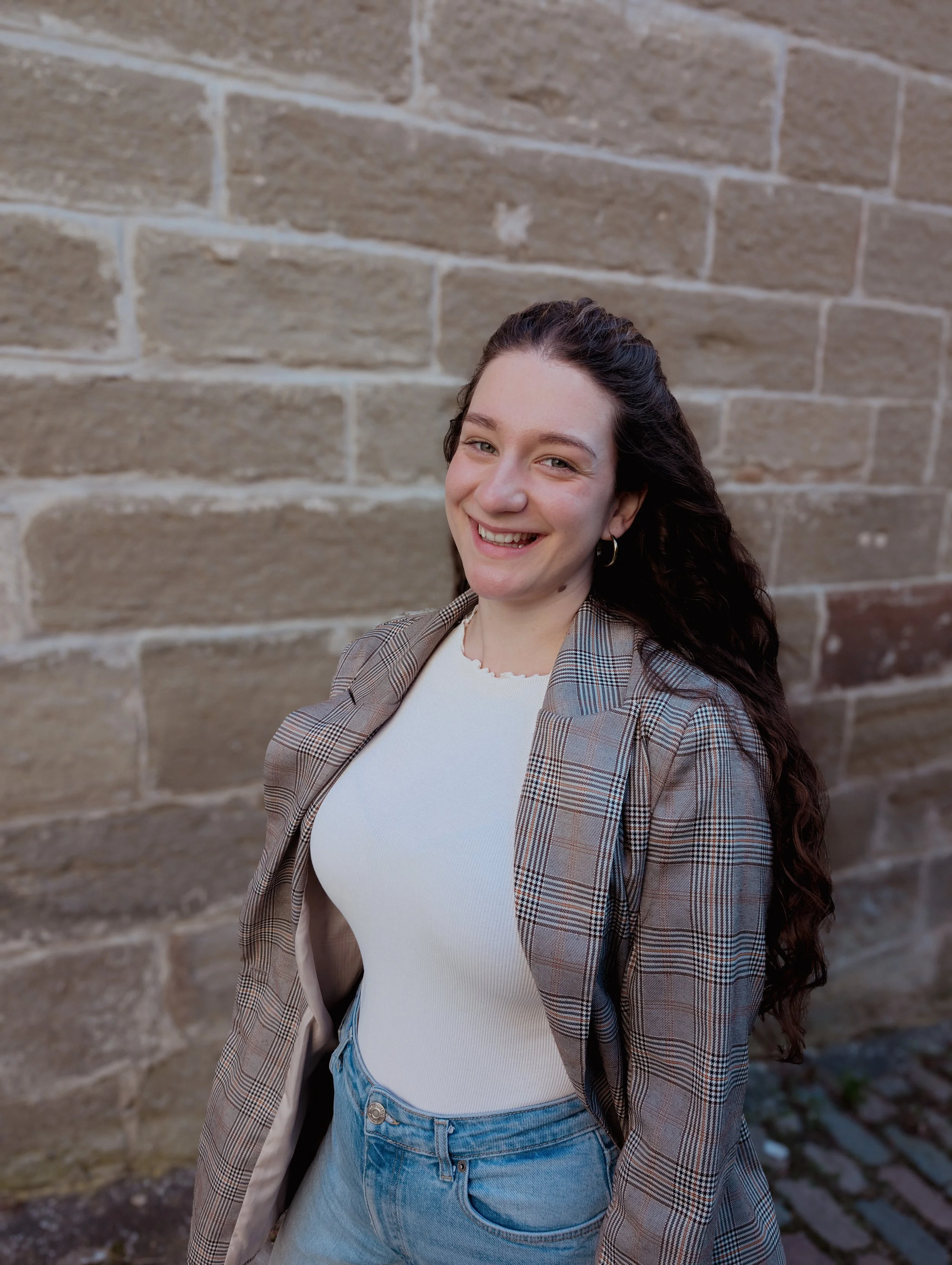 Porträt einer lachenden Freien Traurednerin mit langen, lockigen dunklen Haaren vor einer Ziegelsteinmauer in Herrenberg.