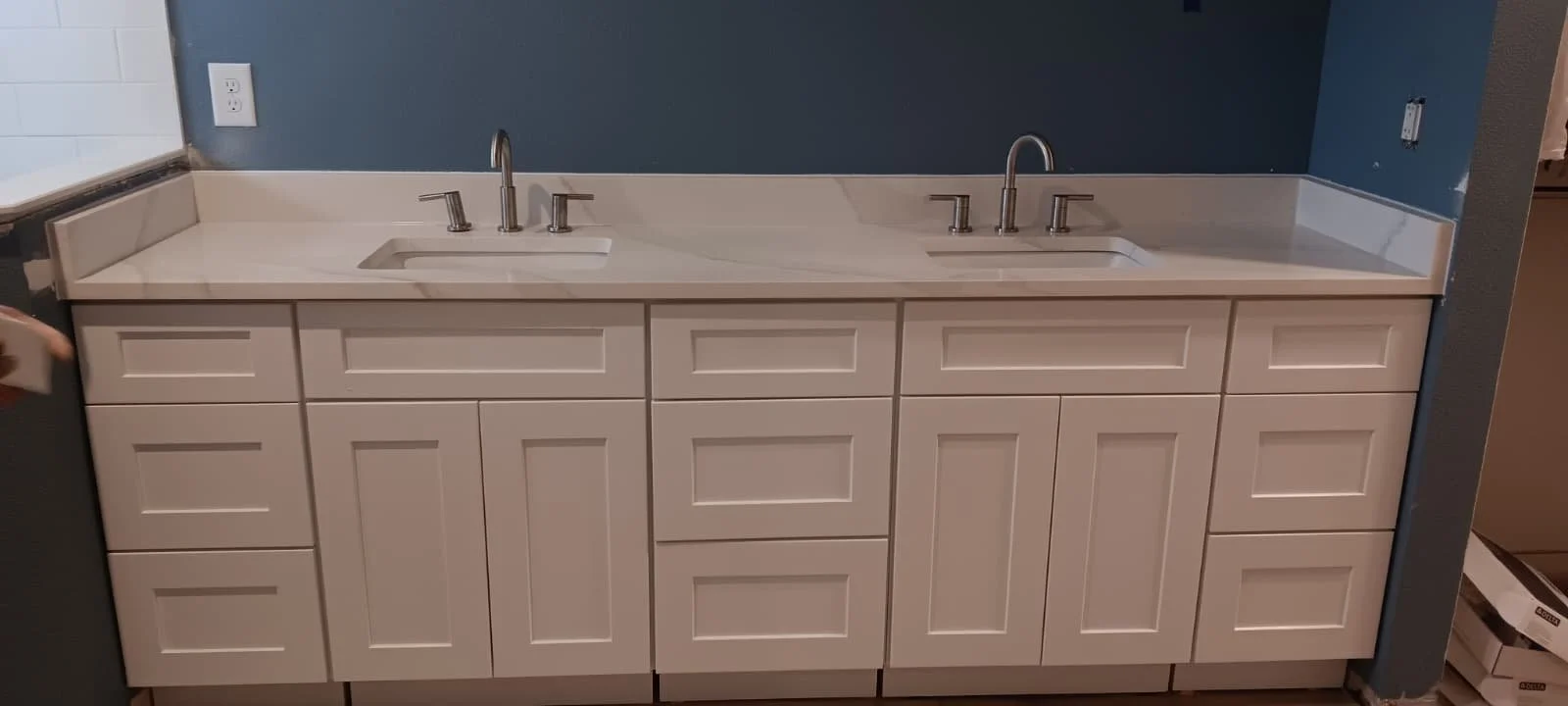 Double kitchen sink with white cabinet and blue wall background.