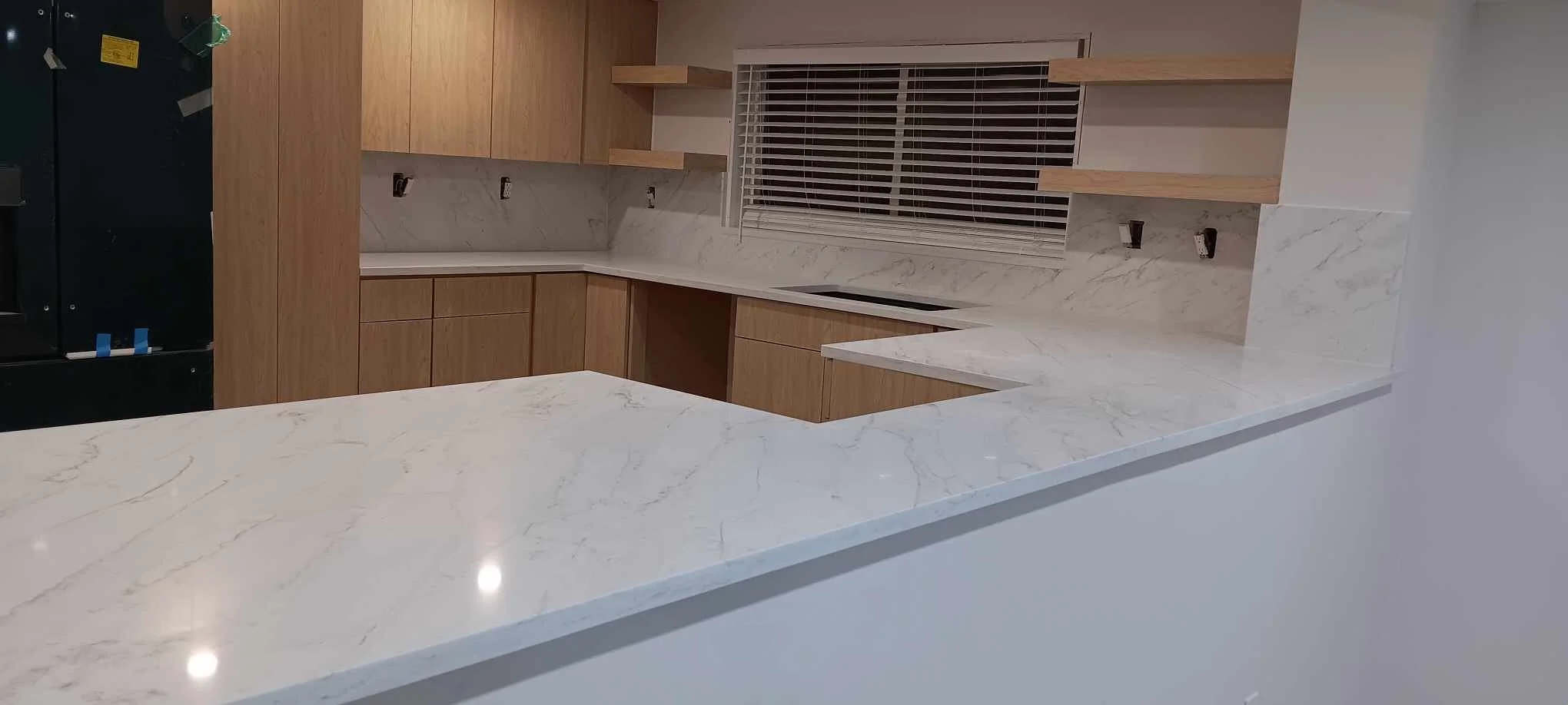 Kitchen with wooden cabinets, marble countertops, and a window with blinds.