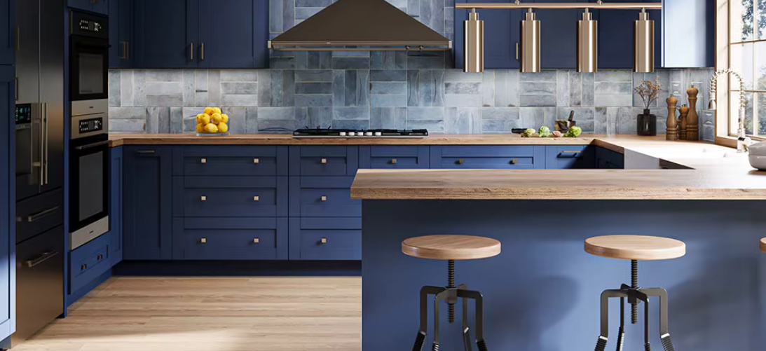 Modern kitchen with blue cabinetry, wooden countertops, and a gray stone backsplash. Two wooden bar stools sit at a counter, with a large window on the right side letting in natural light.