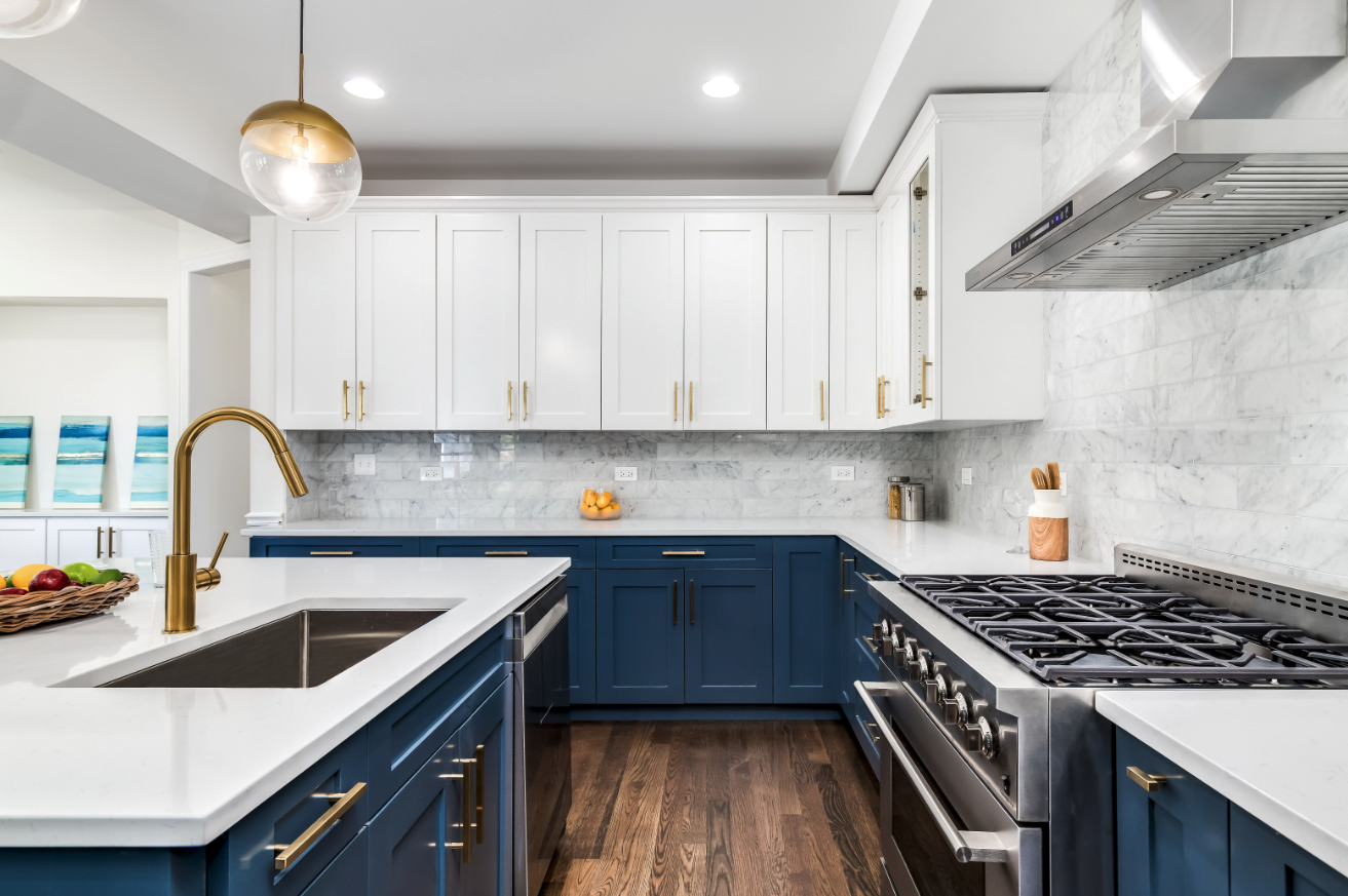 Modern kitchen with white upper cabinets, blue lower cabinets, white marble subway tile backsplash, stainless steel stove, brass faucet, and wooden accents.