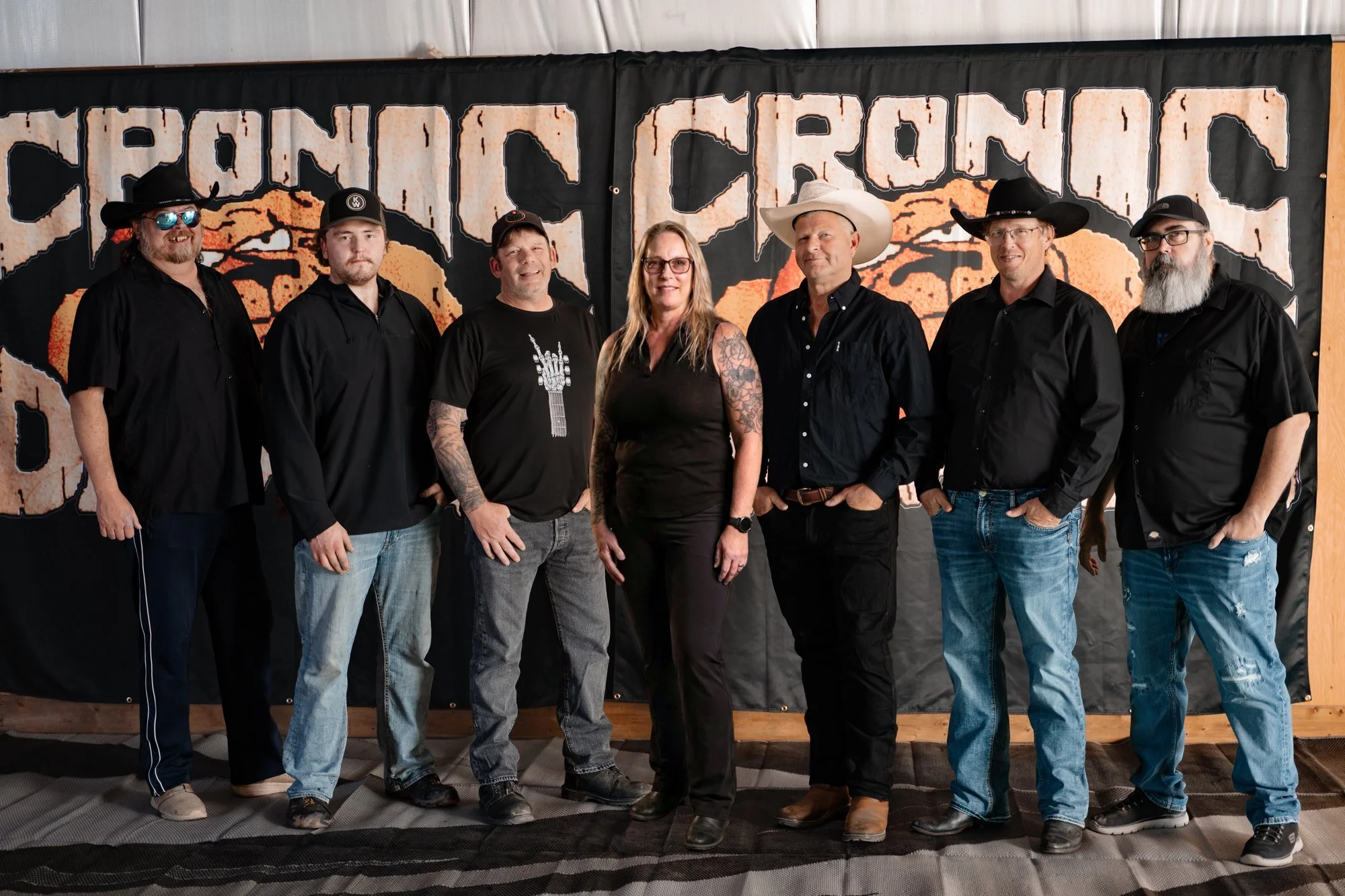 The seven members of Cronic Dawgs, an Alberta party and cover band, standing in front of their bulldog logo banner