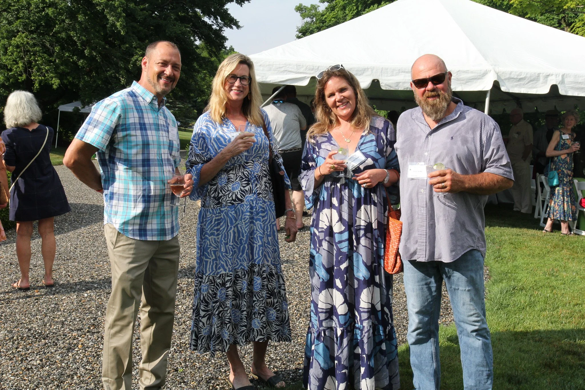 Group of five adults at an outdoor gathering, standing in front of a white tent, holding drinks and smiling.
