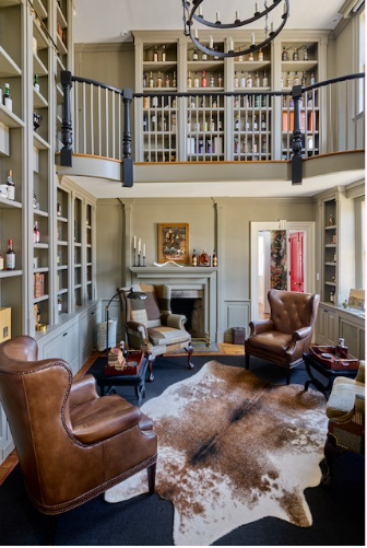 Living room with leather armchairs, a cowhide rug, a fireplace, bookshelves, and a balcony or loft area above.
