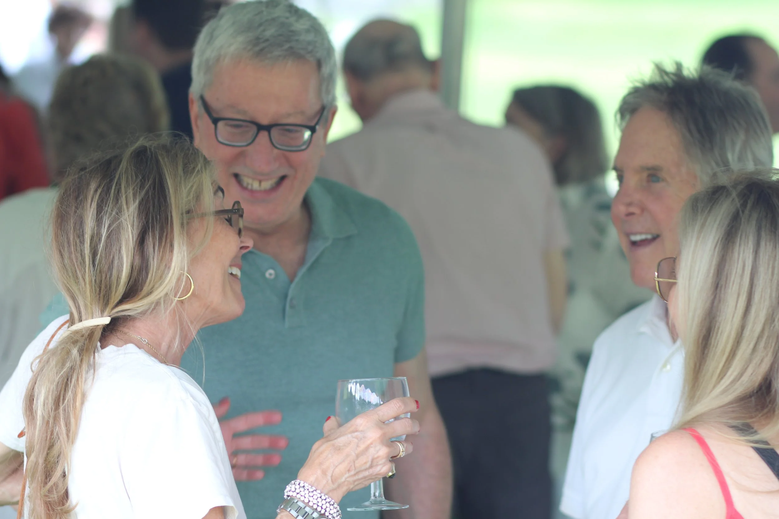 A woman smiling at a man and a couple at a Chore Service fundraiser in Litchfield County