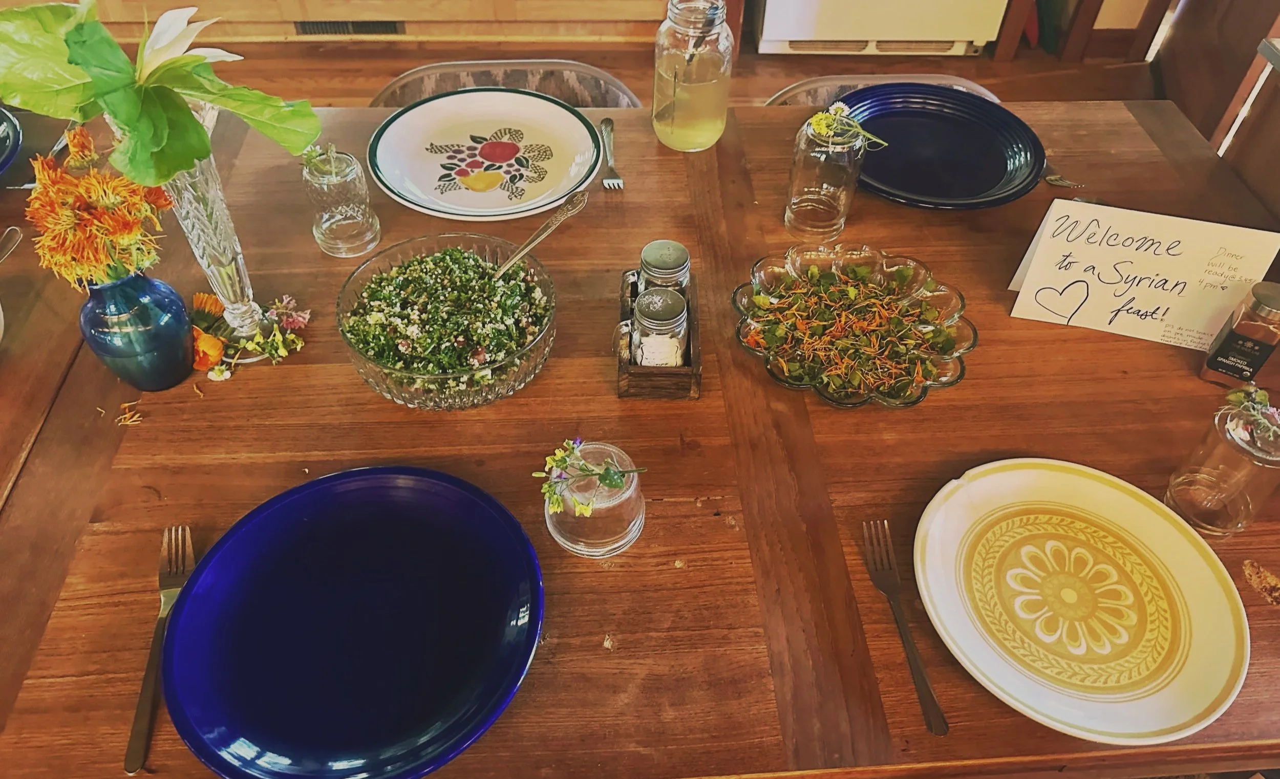 A simple table setting with plates gathered around two central dishes, accented by small vases of greenery bringing life to the scene.