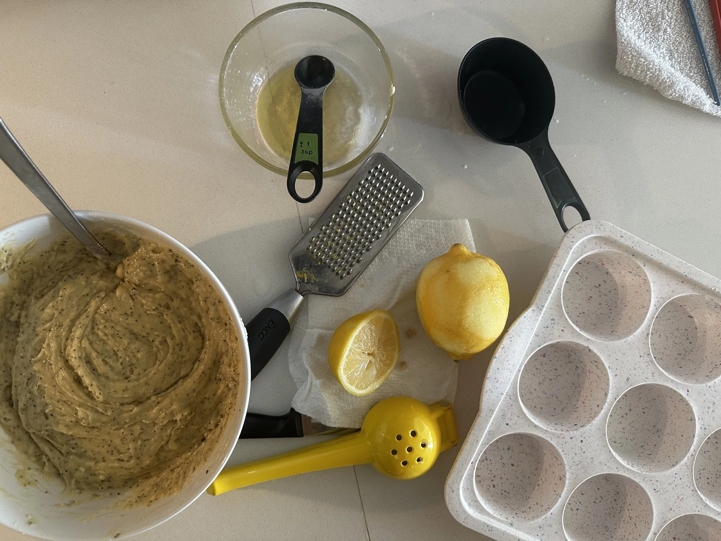 Ingredients for homemade lemon poppy seed muffins laid out on a kitchen counter, including flour, fresh lemons, poppy seeds, and mixing bowls in warm natural light.
