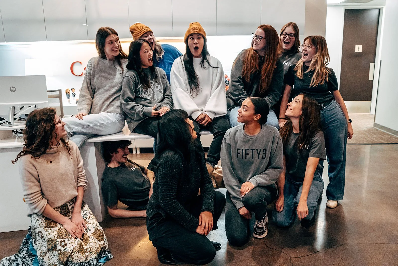 Group of people in casual attire, laughing and interacting in an office setting.