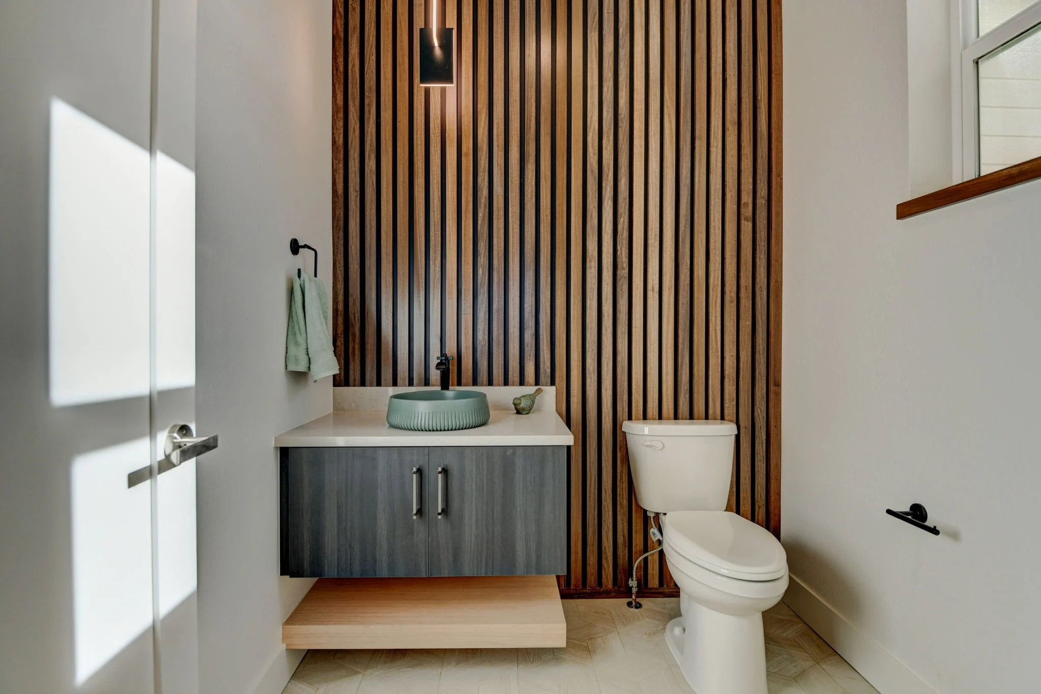 Modern bathroom with a wooden slat accent wall, a floating vanity with a round sink, a wall-mounted faucet, a white toilet, and a towel rack with a green towel.