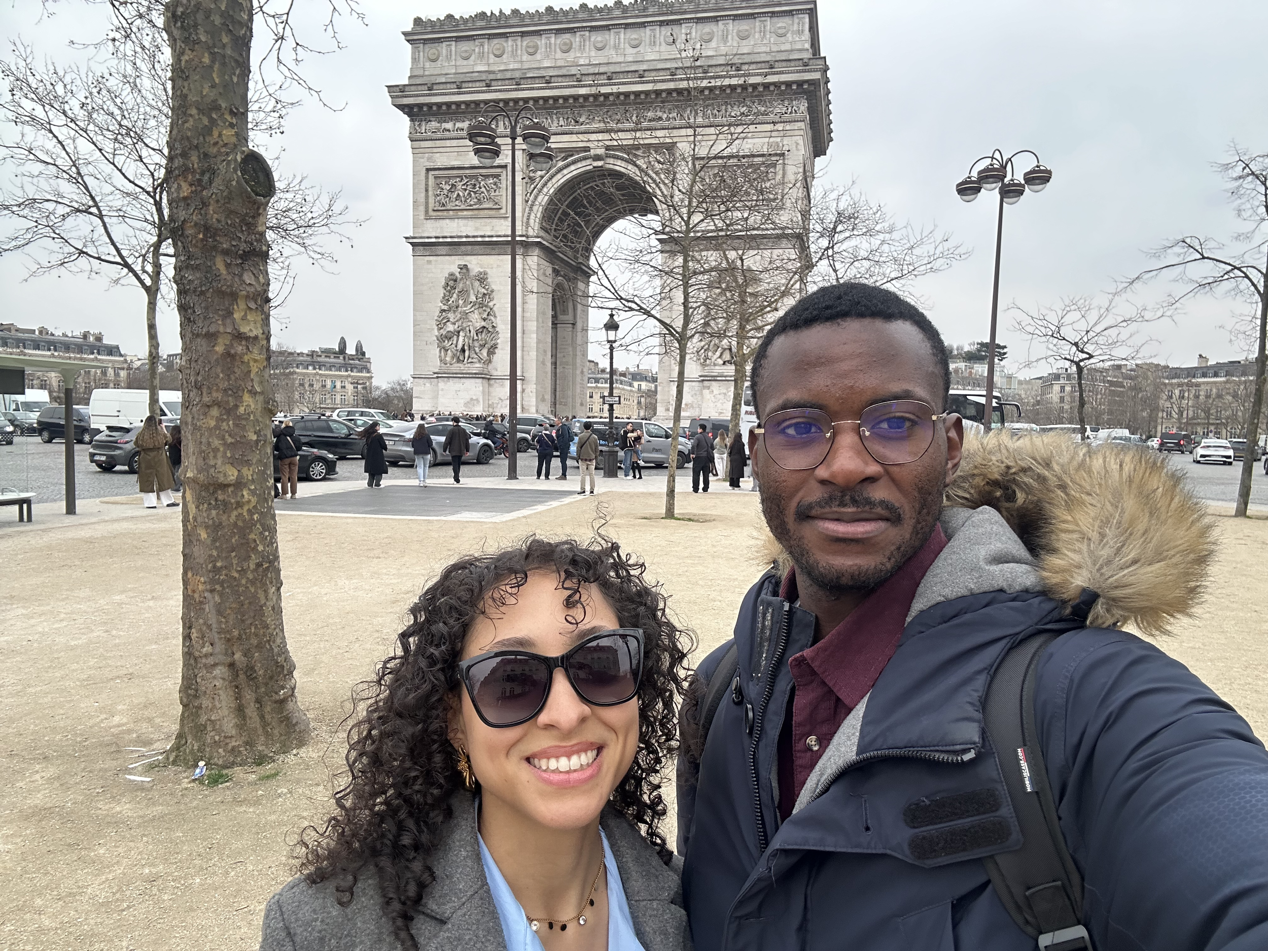 Deux personnes souriantes devant l'Arc de Triomphe à Paris.