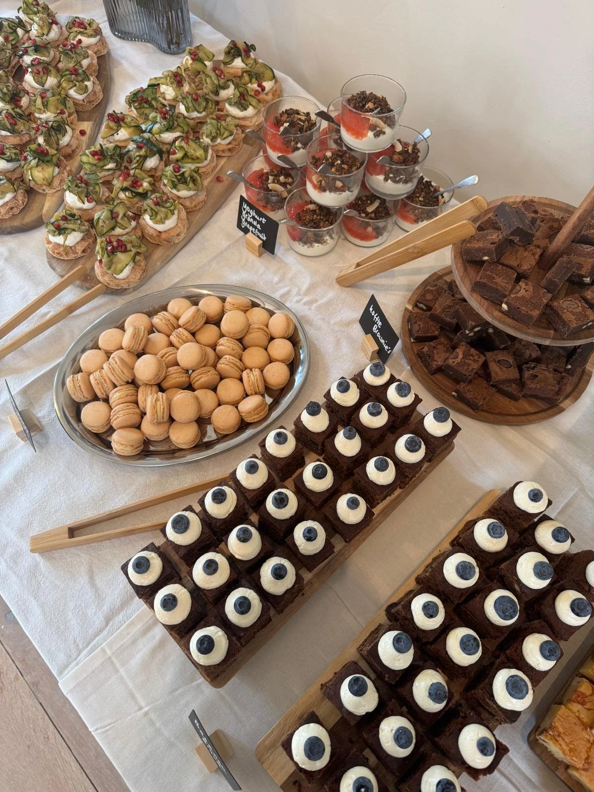 Een tafel met verschillende zoete lekkernijen, waaronder macarons, brownie taartjes met blauwe bessen, en dessertbekers met yoghurt, granola en fruit.