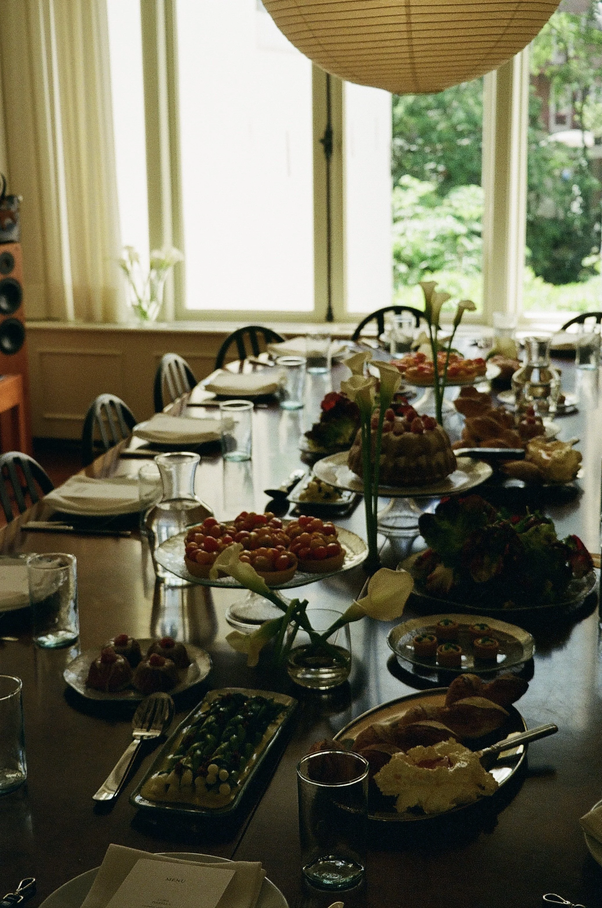 Een feesttafel met diverse desserts en drankjes in een kamer met grote ramen en een groene tuin buiten.