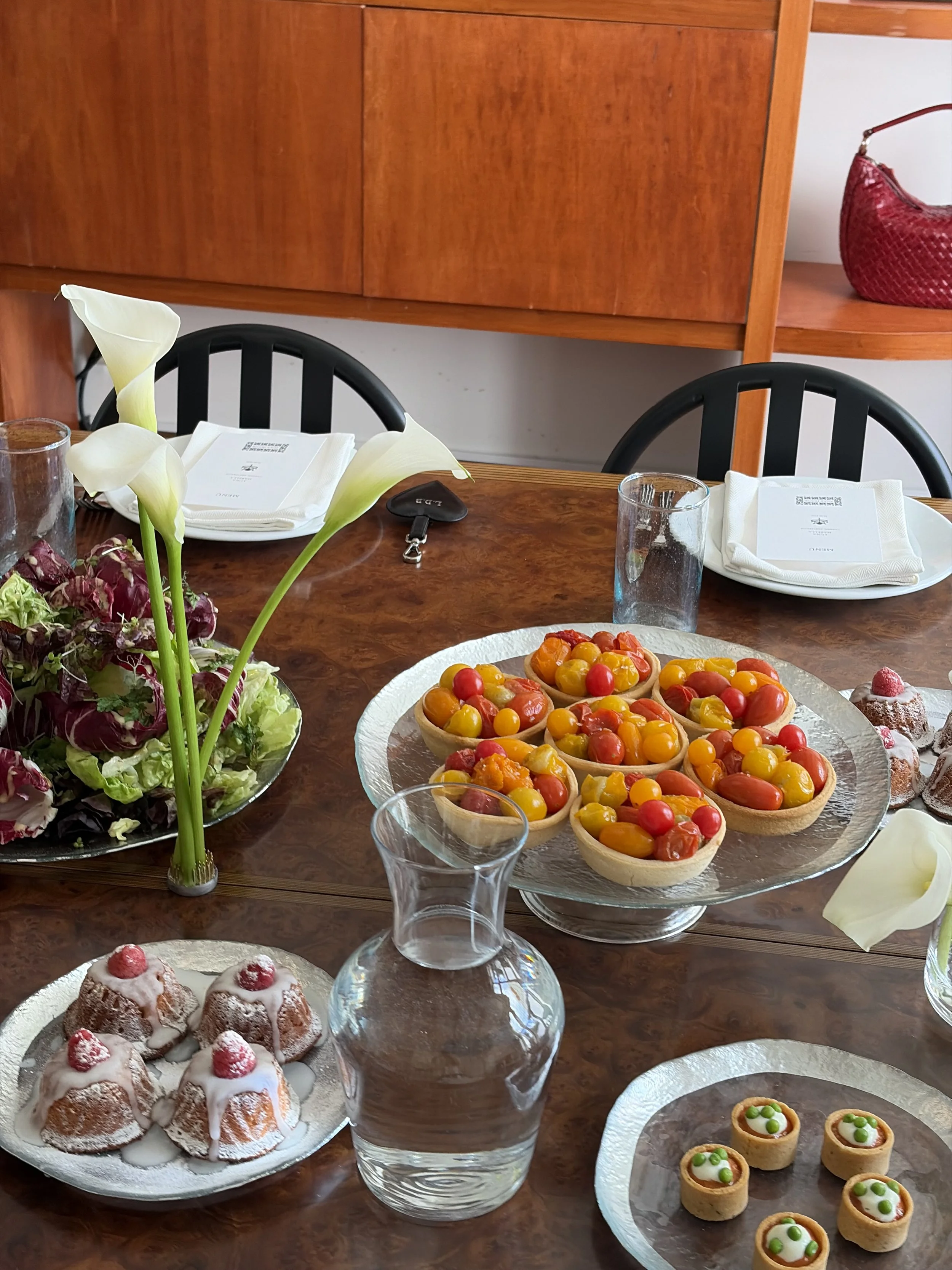 Een gedekte tafel met verschillende desserts, waaronder fruitbavarois, kleine taarten met groenten, en een vaas met witte calla-lilies.